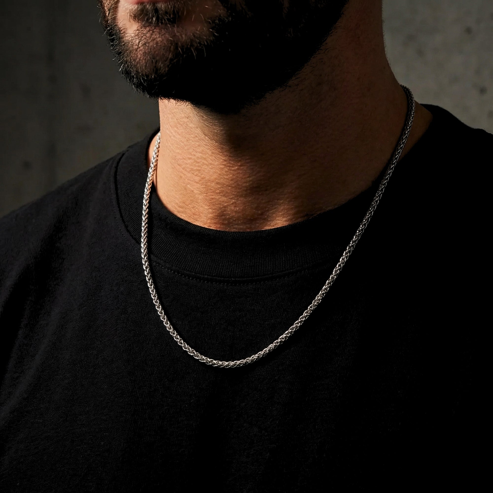 Close-up of a silver stainless steel wheat weave chain necklace on a man's neck.