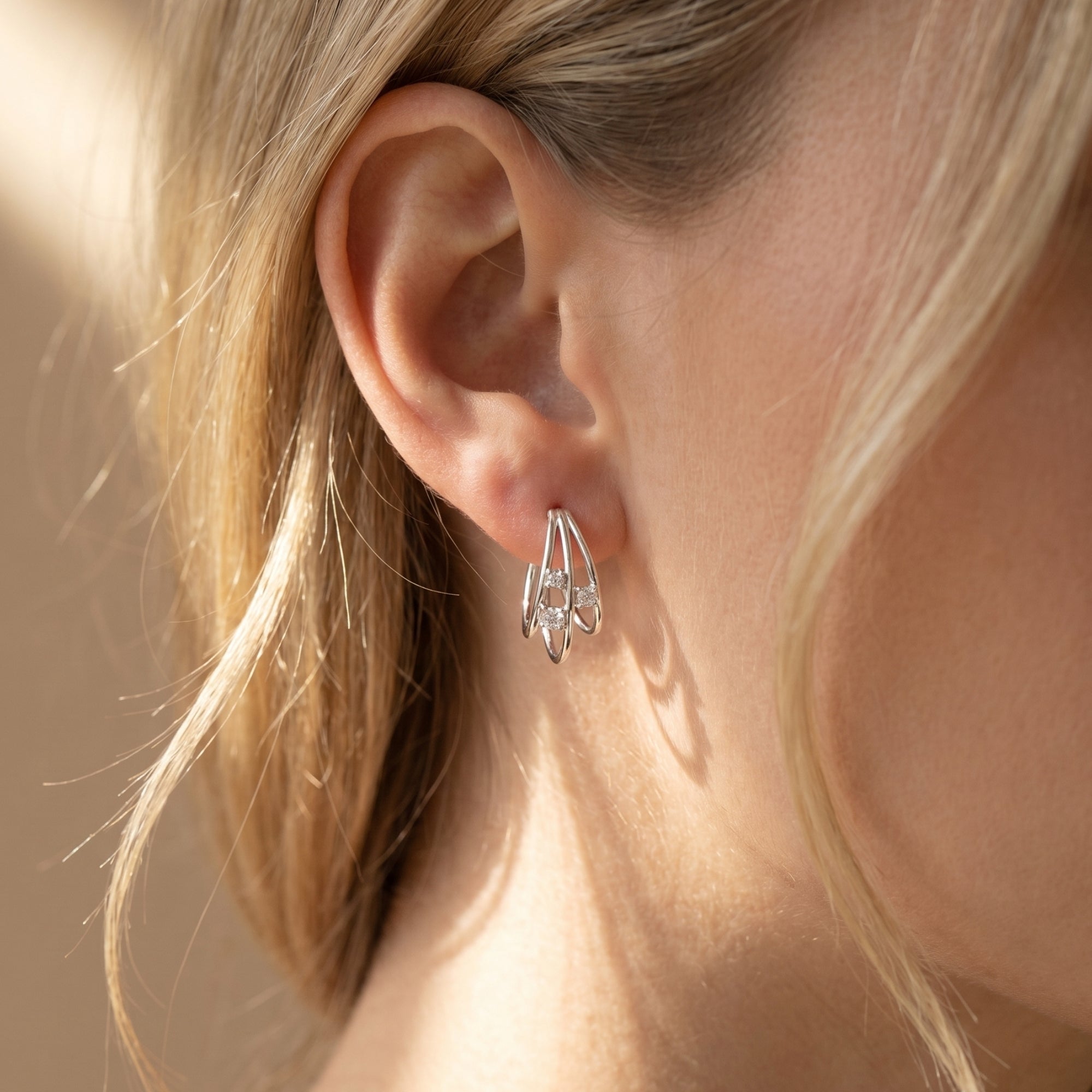 Silver moissanite triple hoop earrings shown worn on a model's ear.