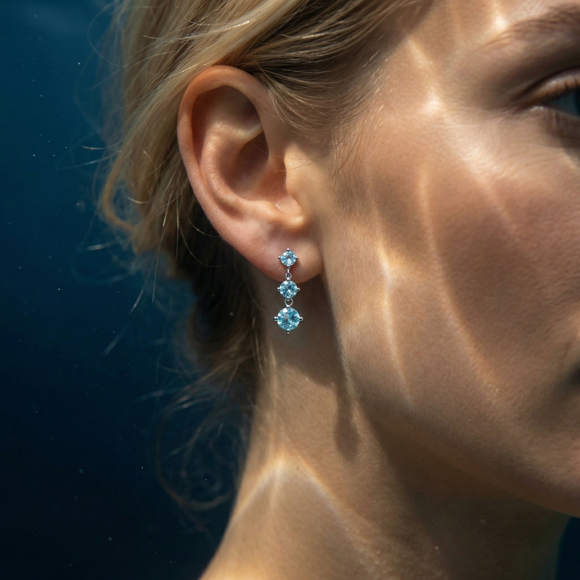 Side view of a model wearing the Cyanea platinum drop earrings featuring three graduating round natural aquamarines.