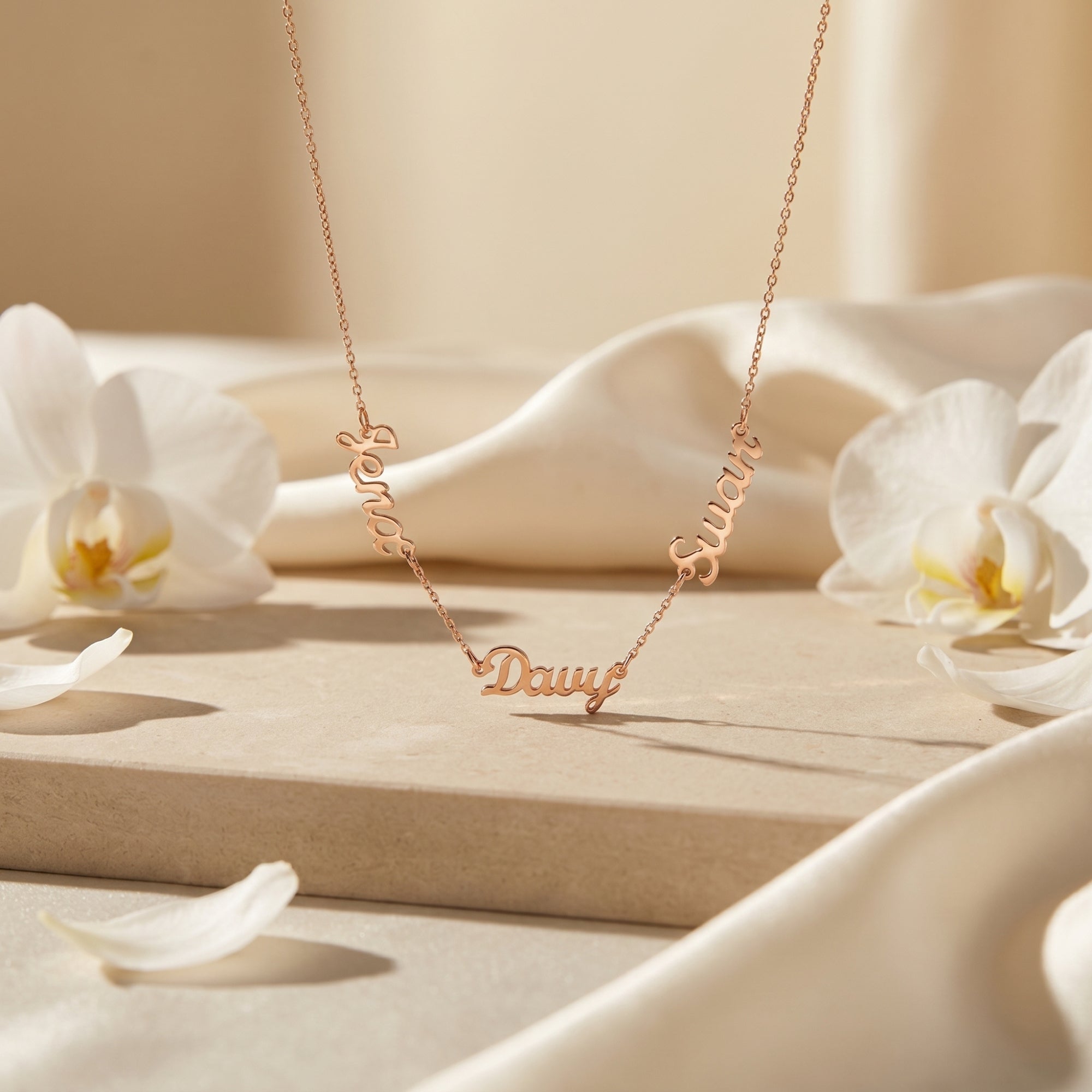 Gold PVD stainless steel name necklace hanging over a stone surface with orchids.