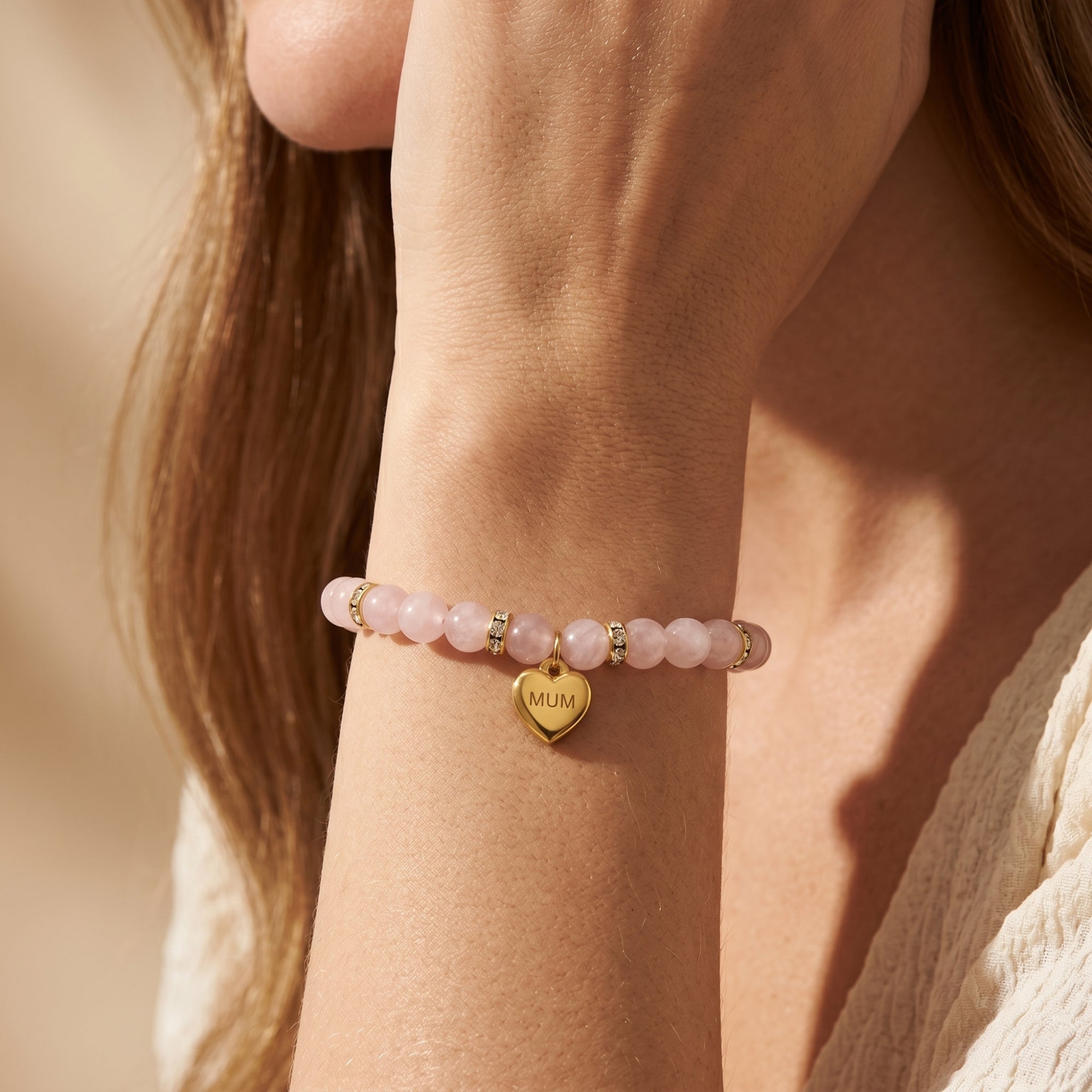 Close-up of the gold rose quartz bracelet and engraved MUM heart charm on a model's wrist.