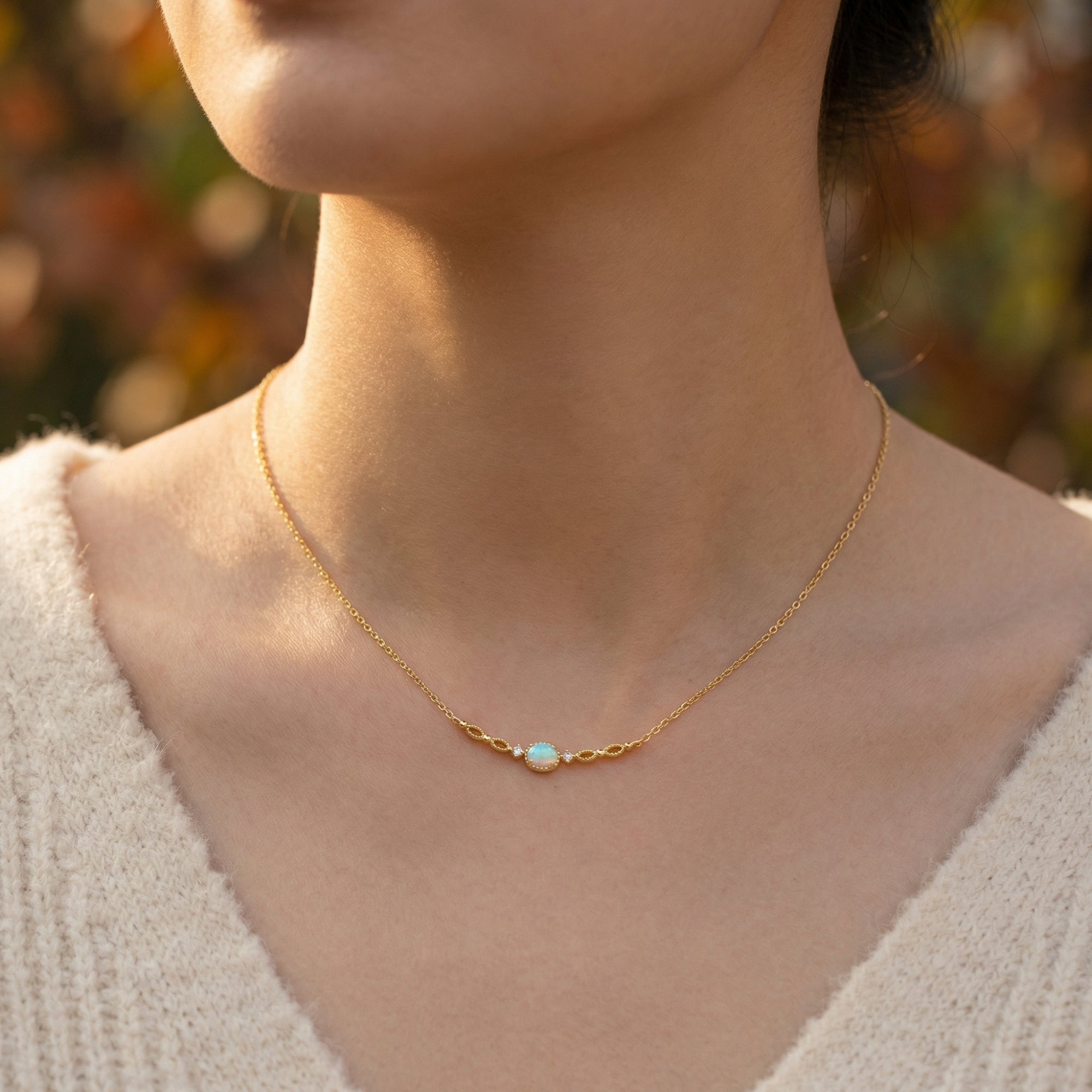 Front view of a model wearing the gold-tone Lumisara necklace featuring an oval white opal pendant.