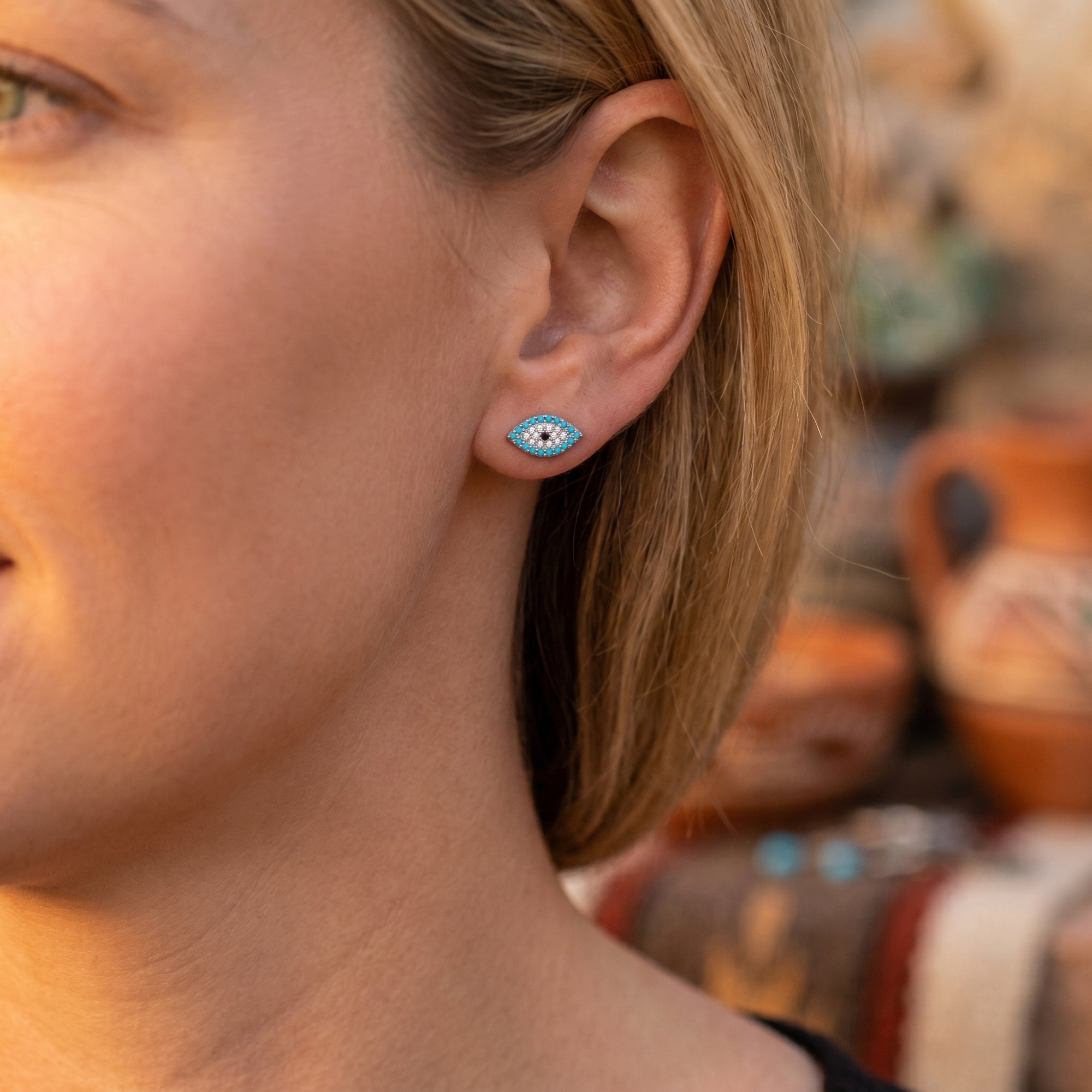 Side view of a woman wearing a silver turquoise evil eye stud earring with a Southwestern desert background.