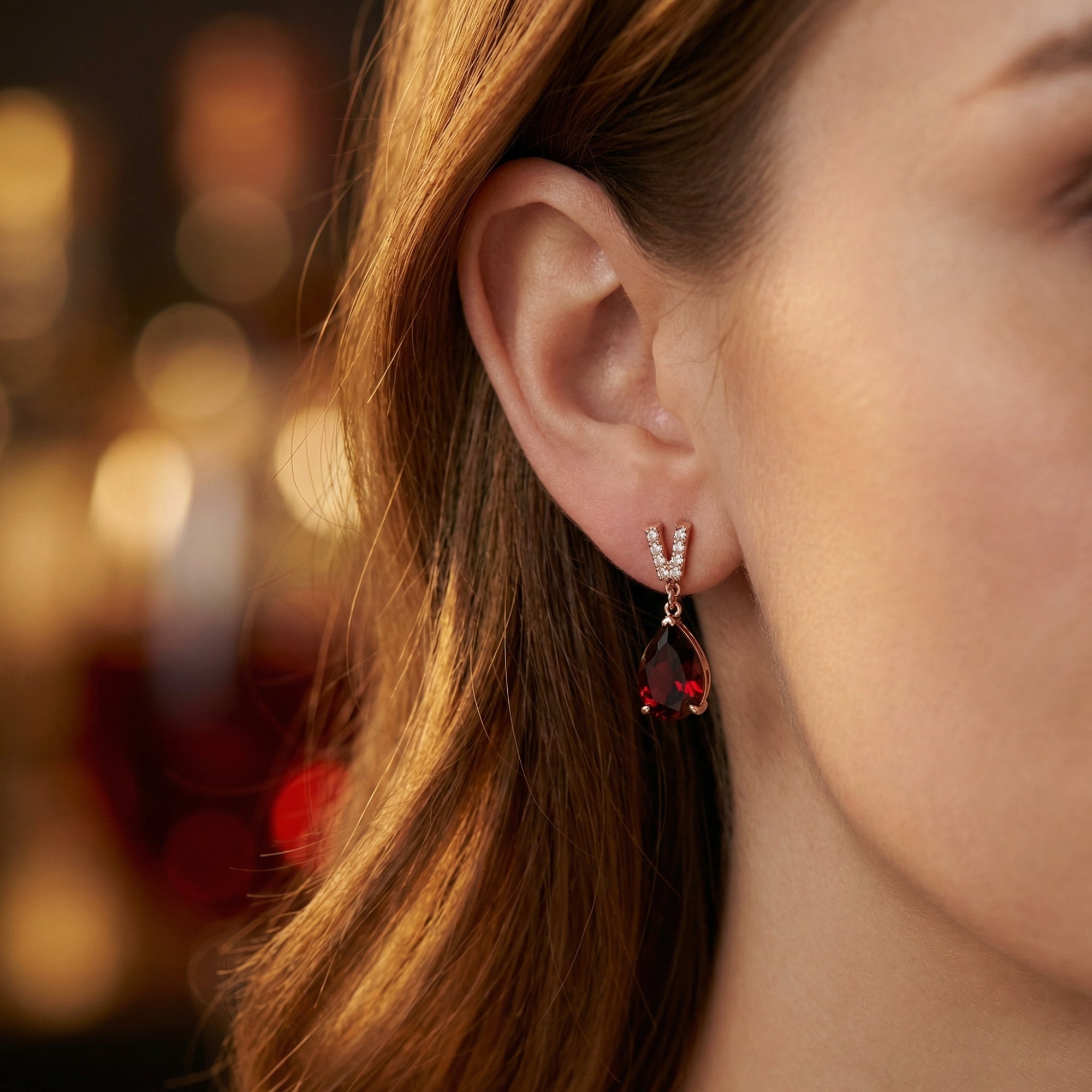 Side view of the Olyndra pear drop earring in 18K rose gold with a pear-cut garnet on a model.