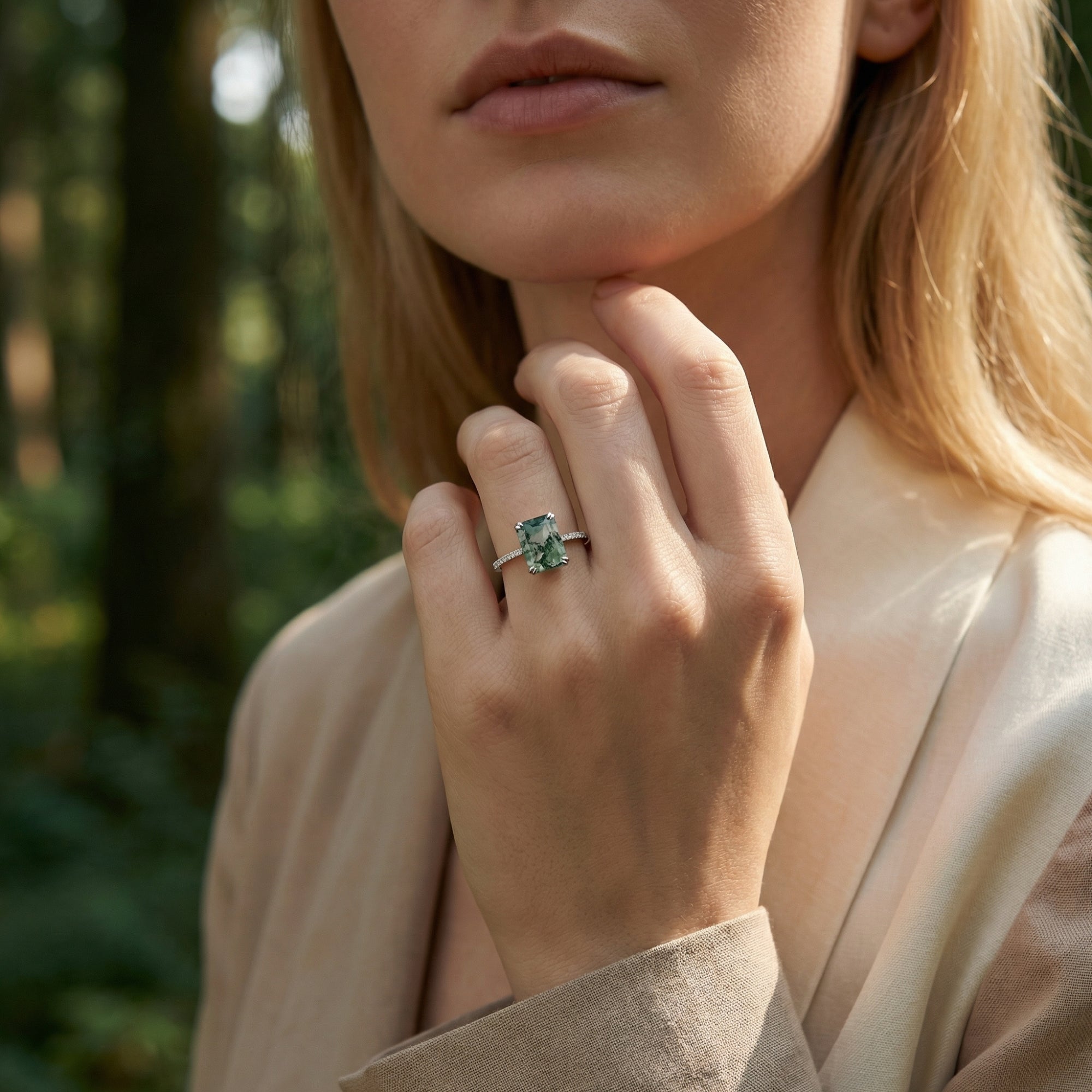 A woman wearing a rectangular moss agate ring in S925 sterling silver on her finger in an outdoor forest environment.