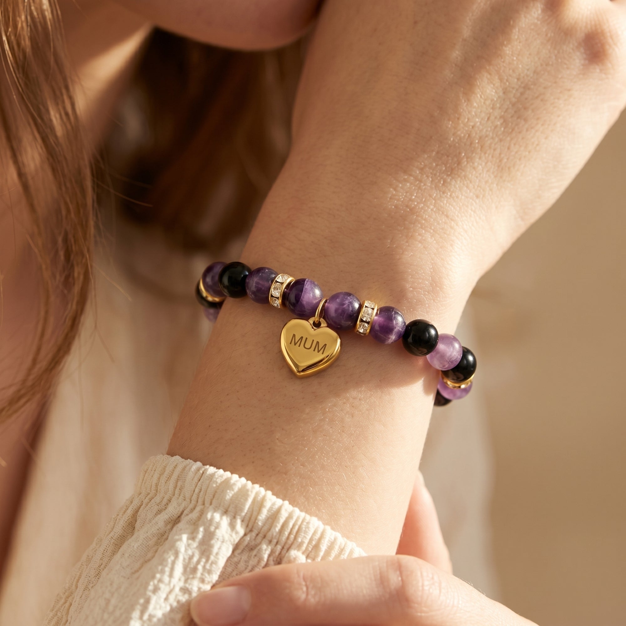 Detail of amethyst beaded bracelet with gold heart charm on a model's wrist.