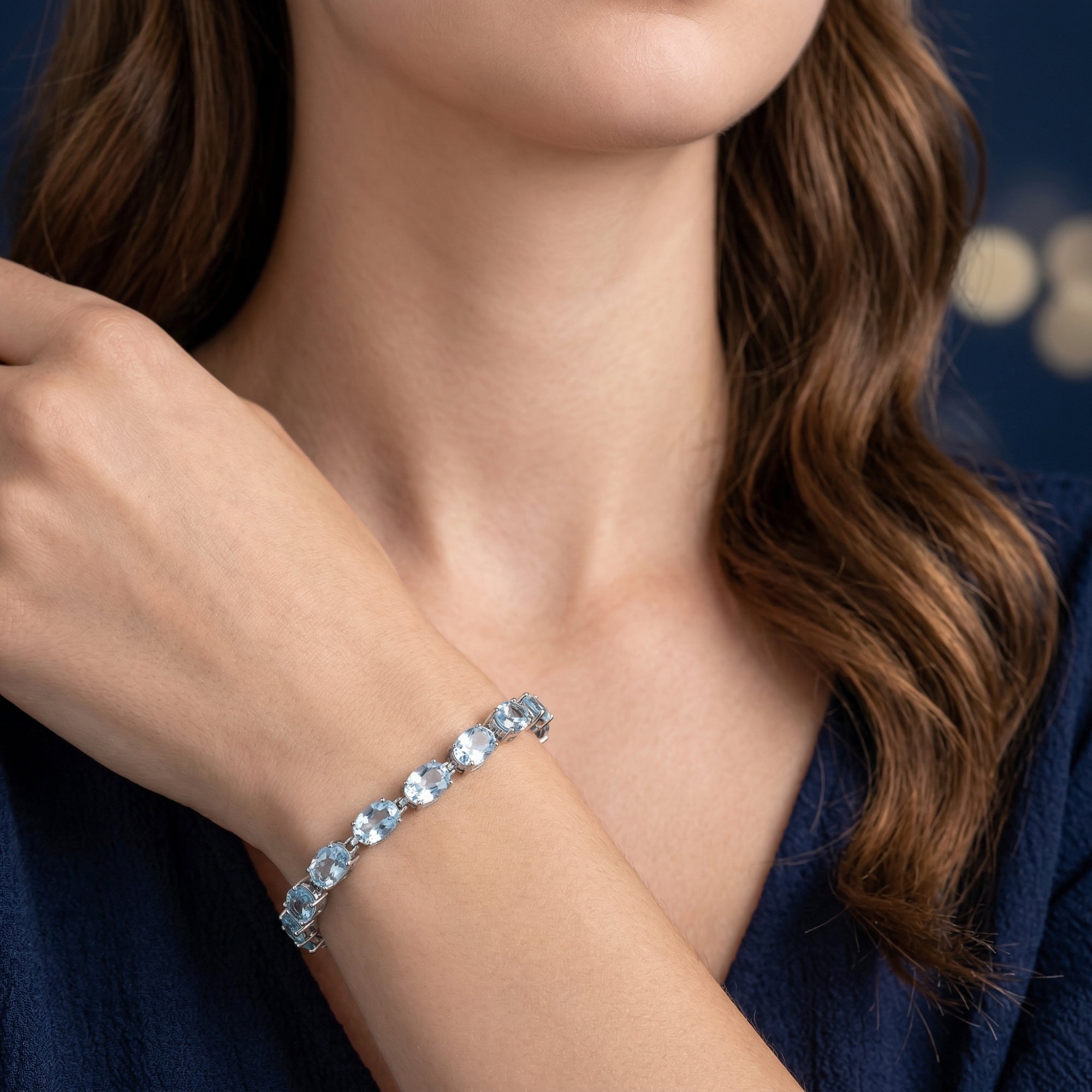 Aquadora blue topaz tennis bracelet in white gold worn on a model's wrist against a dark blue background.