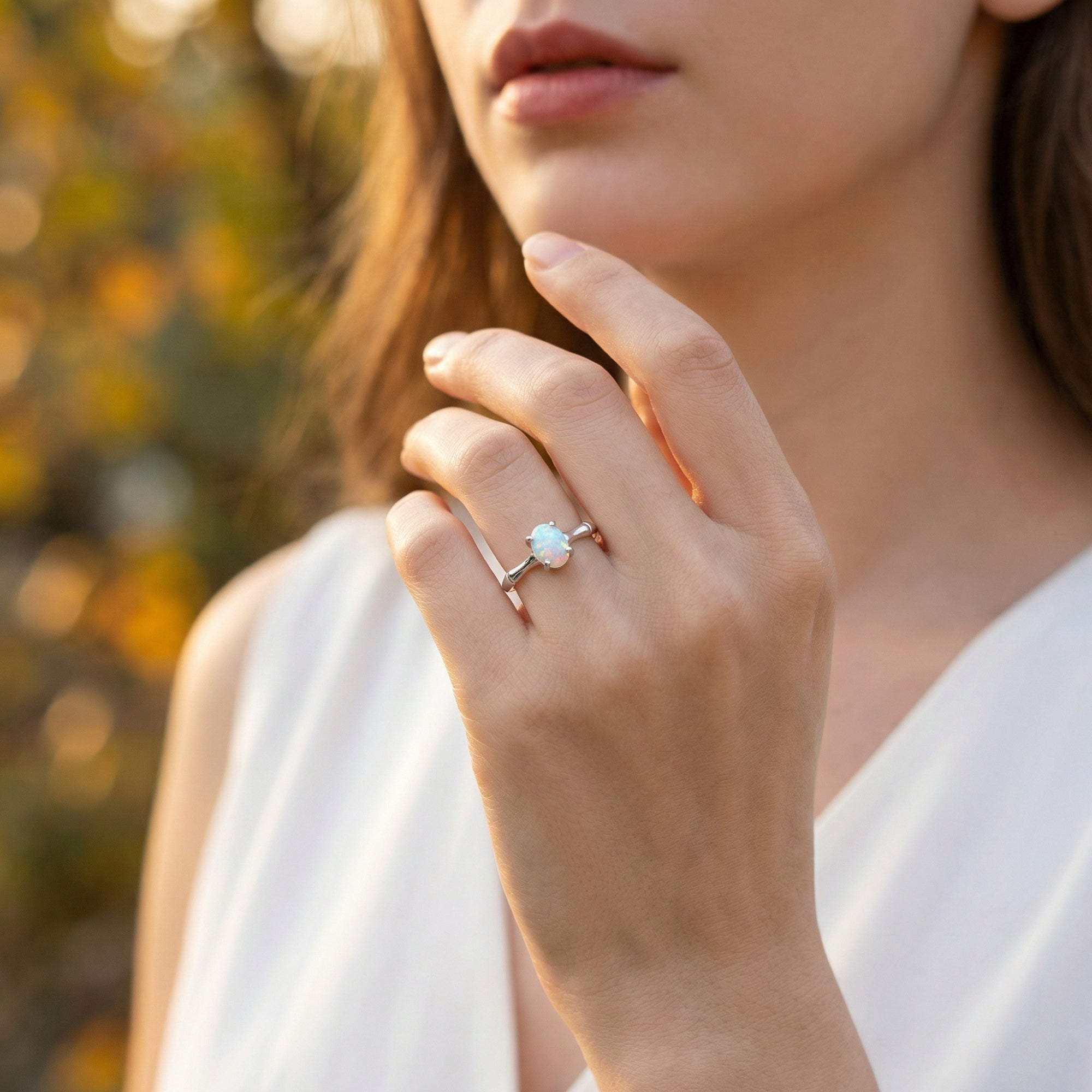Close-up of a model wearing the oval-cut natural opal ring in sterling silver on her finger outdoors.
