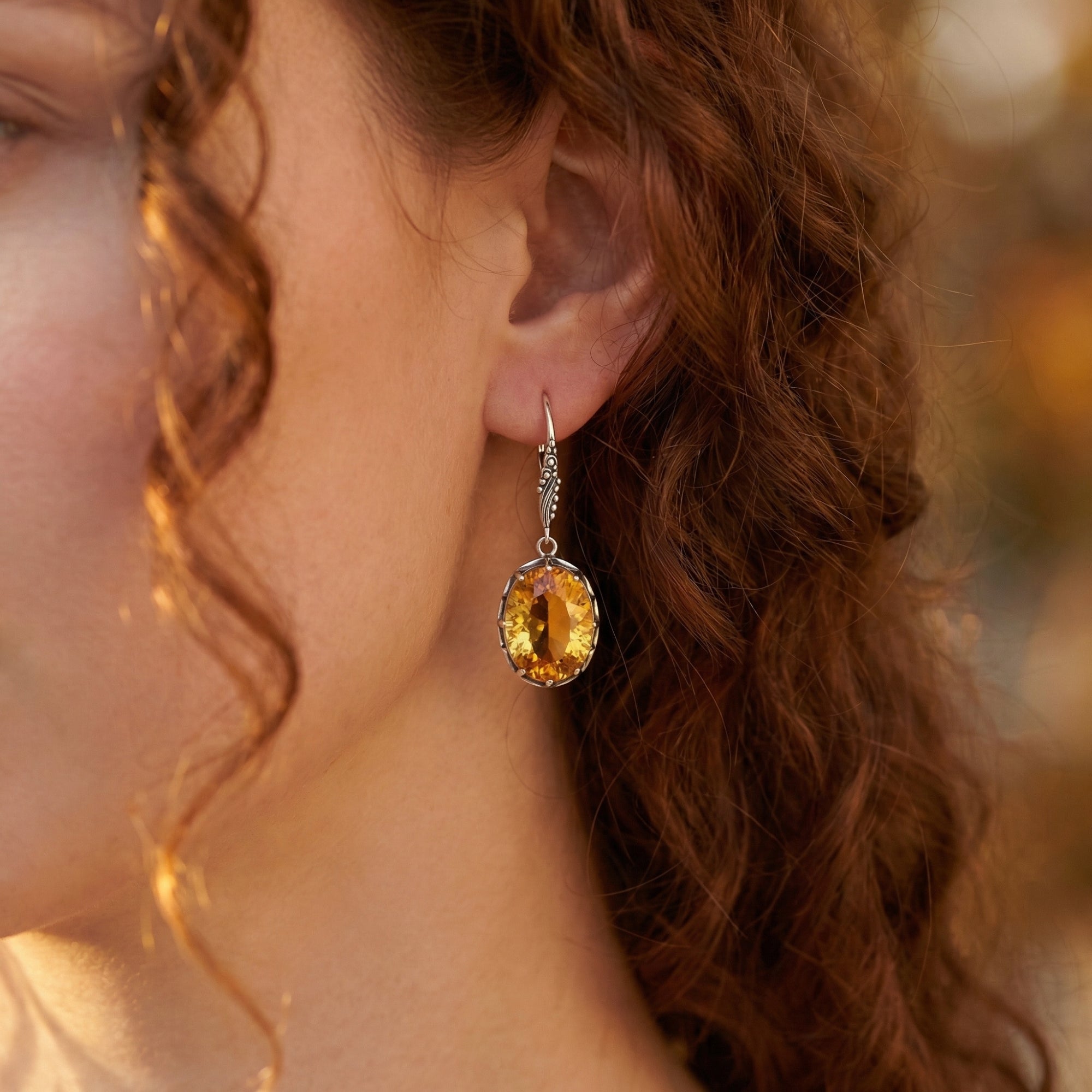 Side view of a model wearing a silver oval cut citrine drop earring with warm outdoor lighting.