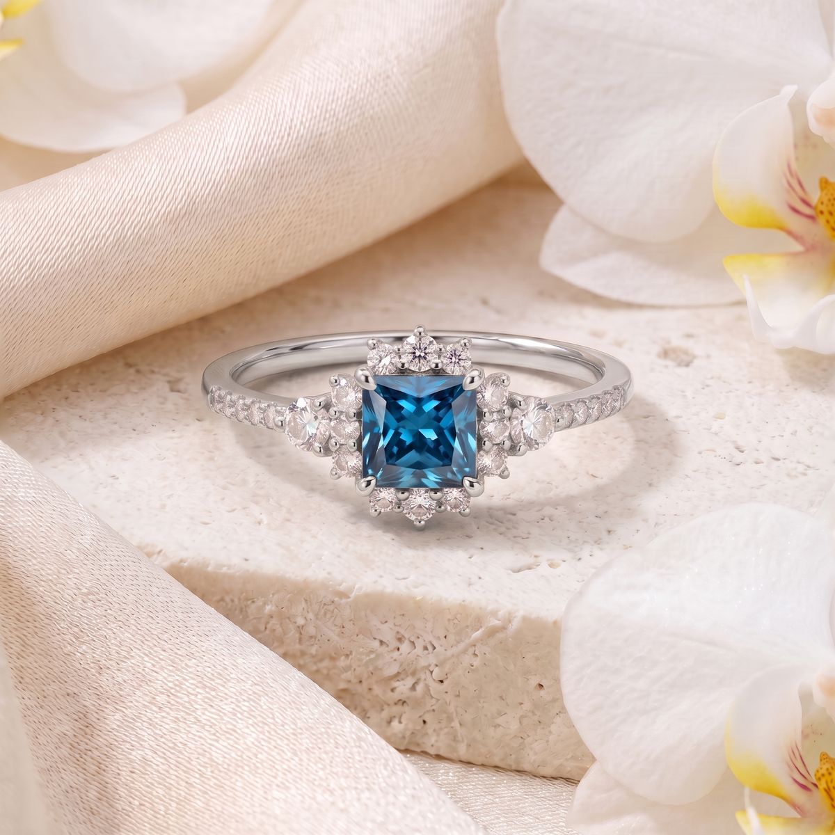 White gold princess cut teal blue moissanite halo ring displayed on a textured stone block.