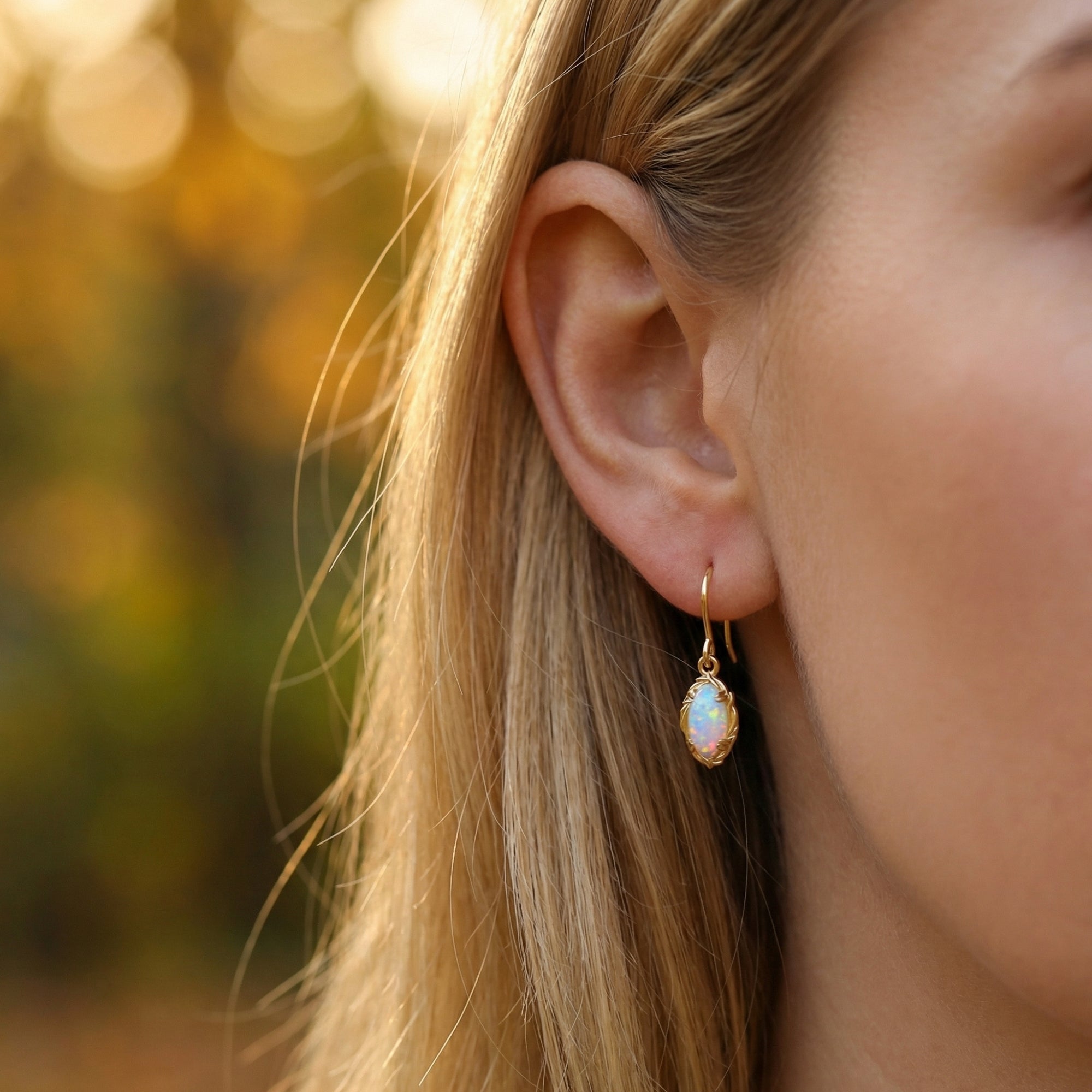 Profile view of a woman wearing the Illumira yellow gold drop earrings with marquise-cut white opals.