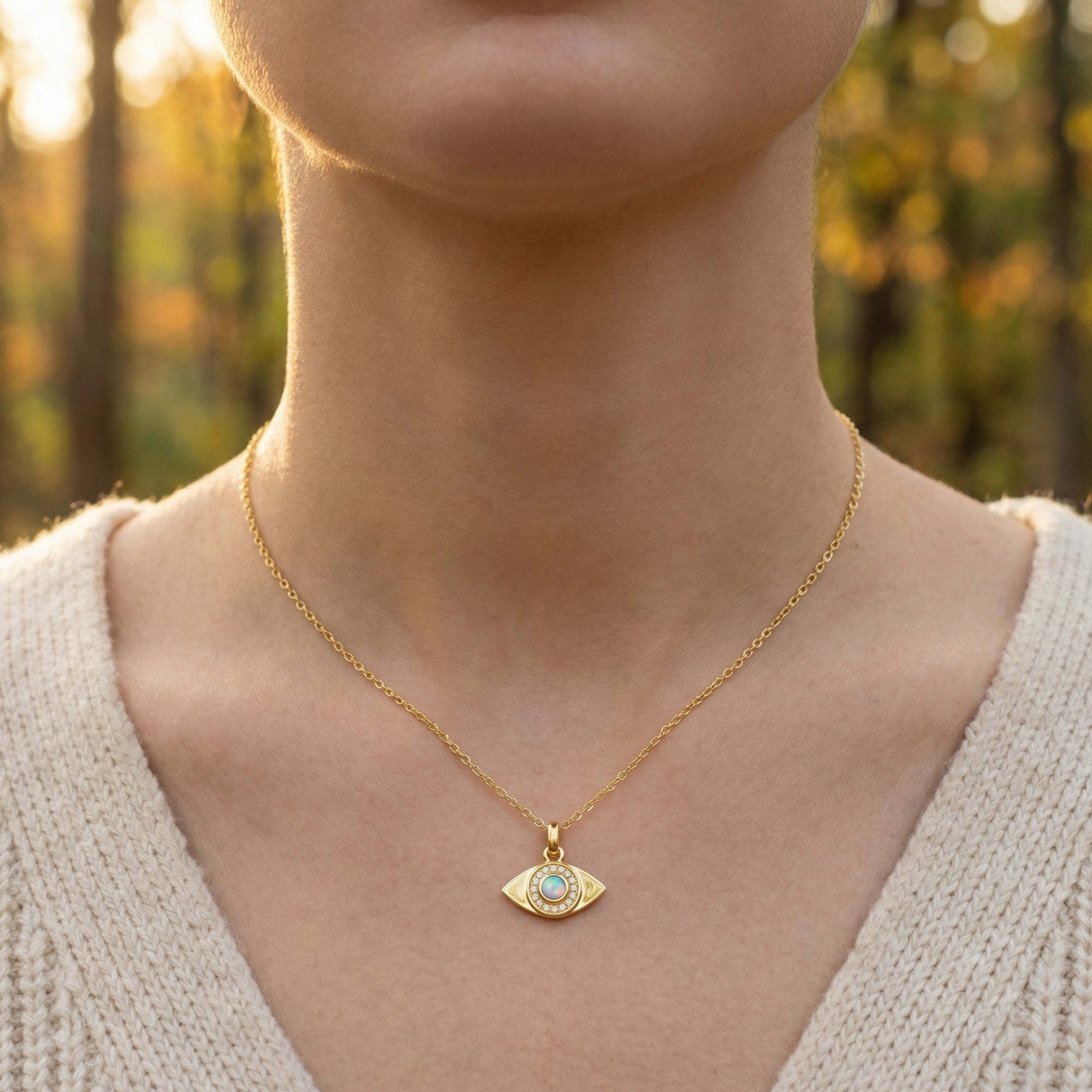 Front view of a woman wearing the gold white opal evil eye pendant necklace over a beige knit sweater.