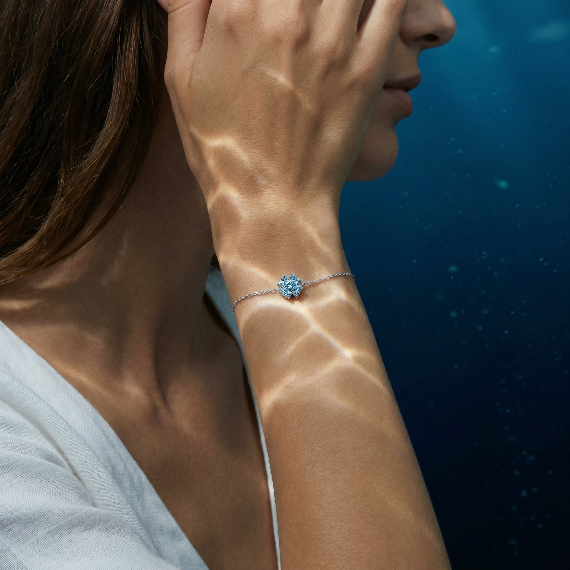 Woman wearing the Marea heart aquamarine platinum bracelet on her wrist under shimmering light.