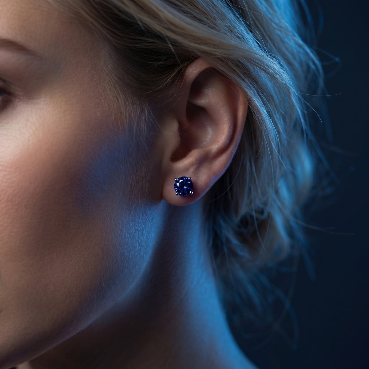 Side profile of a model wearing a deep blue round tanzanite stud earring in 18K white gold.