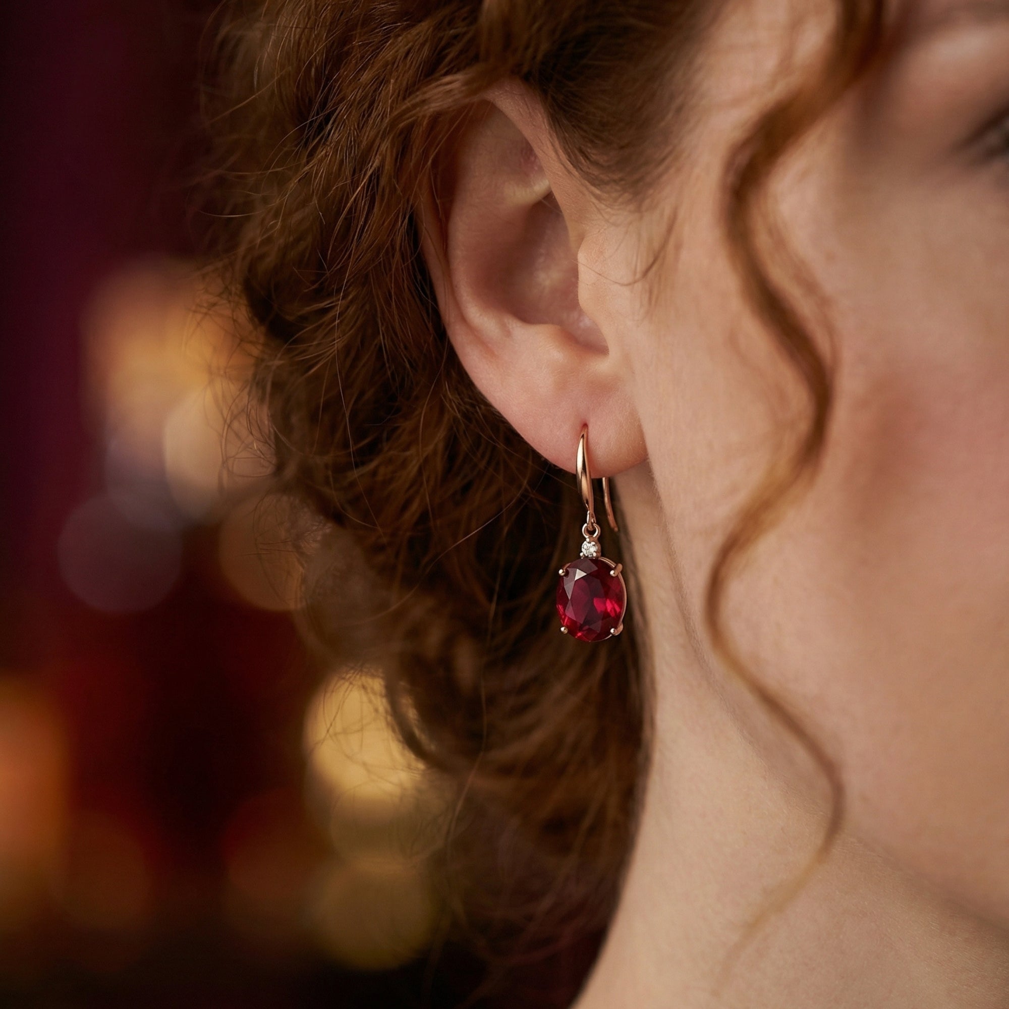 Close-up of a model wearing an 18K rose gold drop earring with an oval cut natural red garnet.