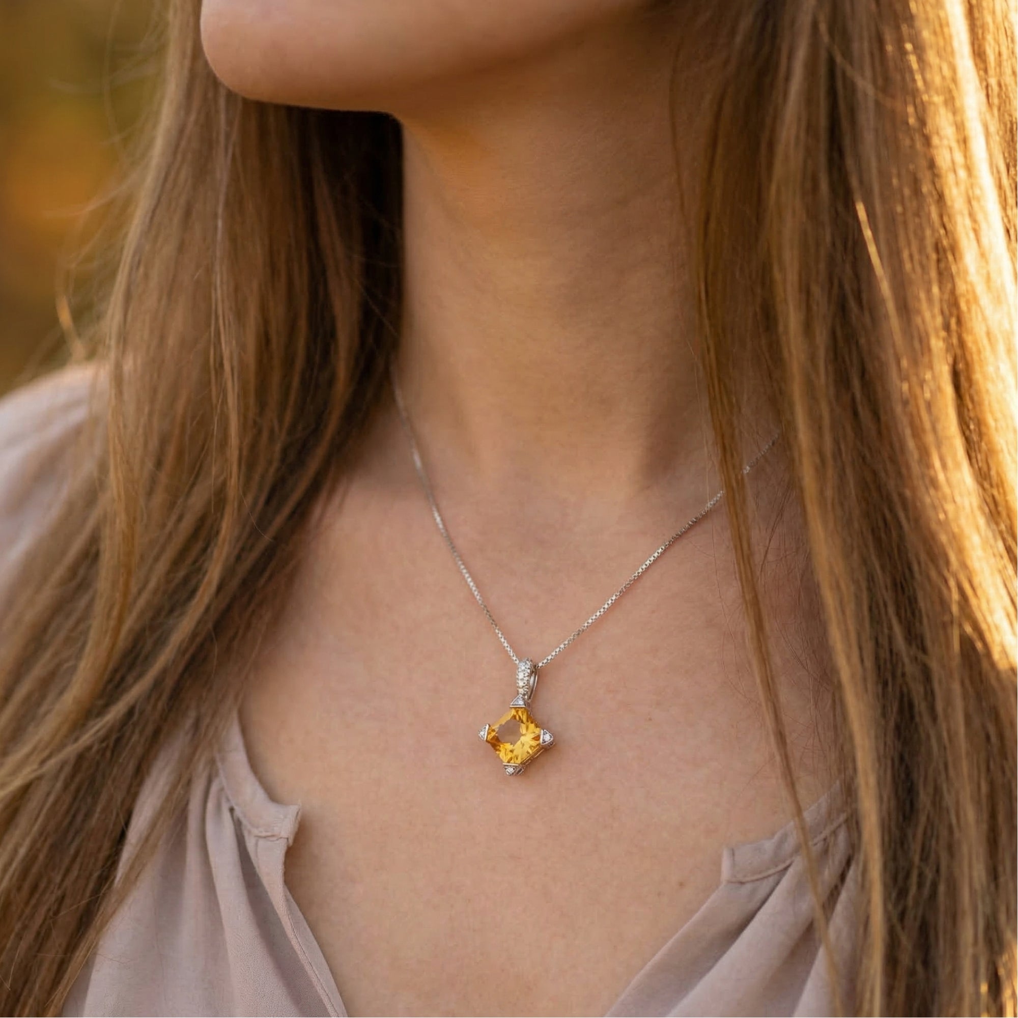 Natural square-cut citrine pendant on a silver chain worn by a woman, capturing the light in an outdoor setting.