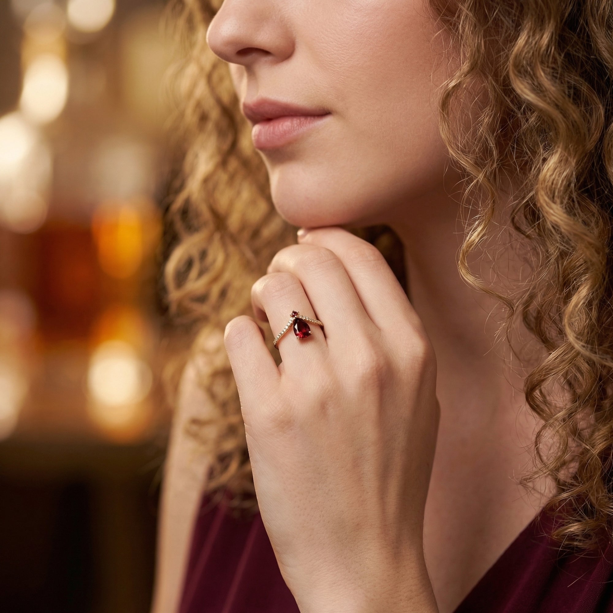 A woman wearing the gold vermeil pear-cut garnet chevron ring, styled with a matching burgundy silk dress.