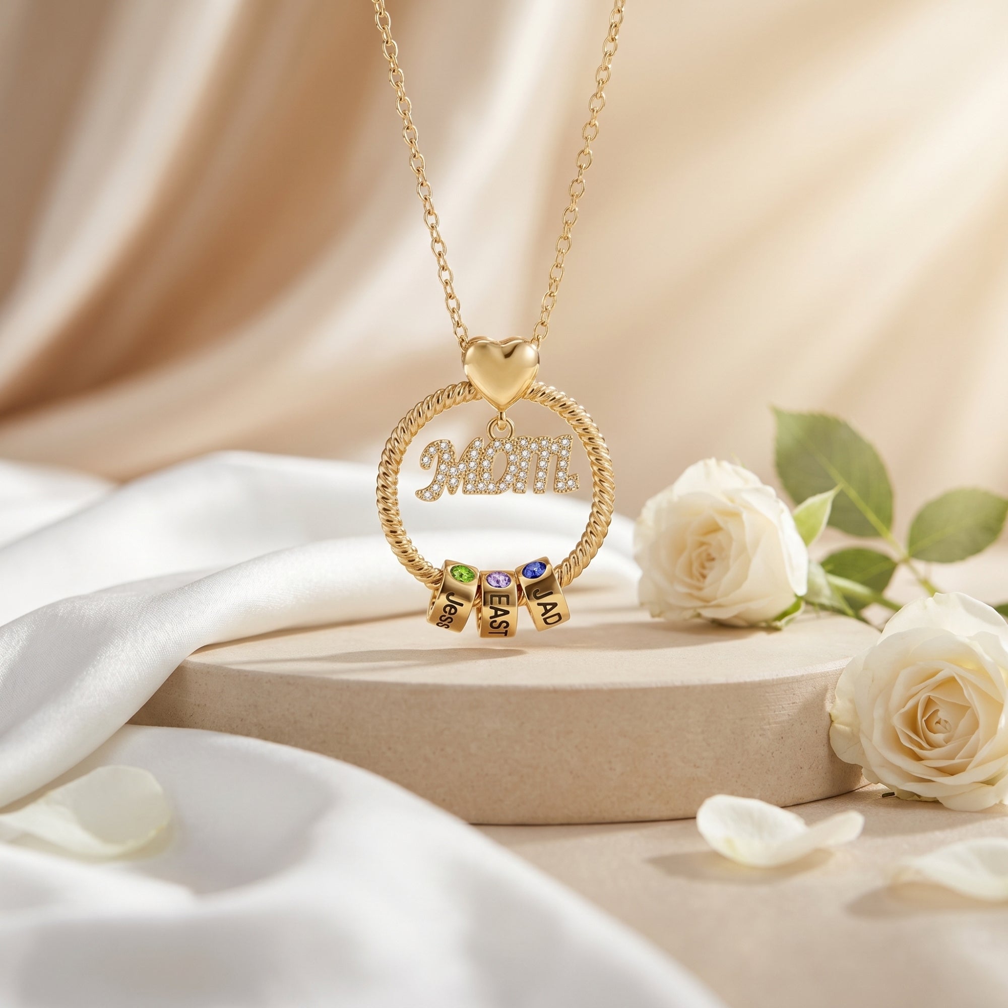 Gold Kalisene necklace featuring a MOM pendant and three engraved birthstone rollers on a display stand.