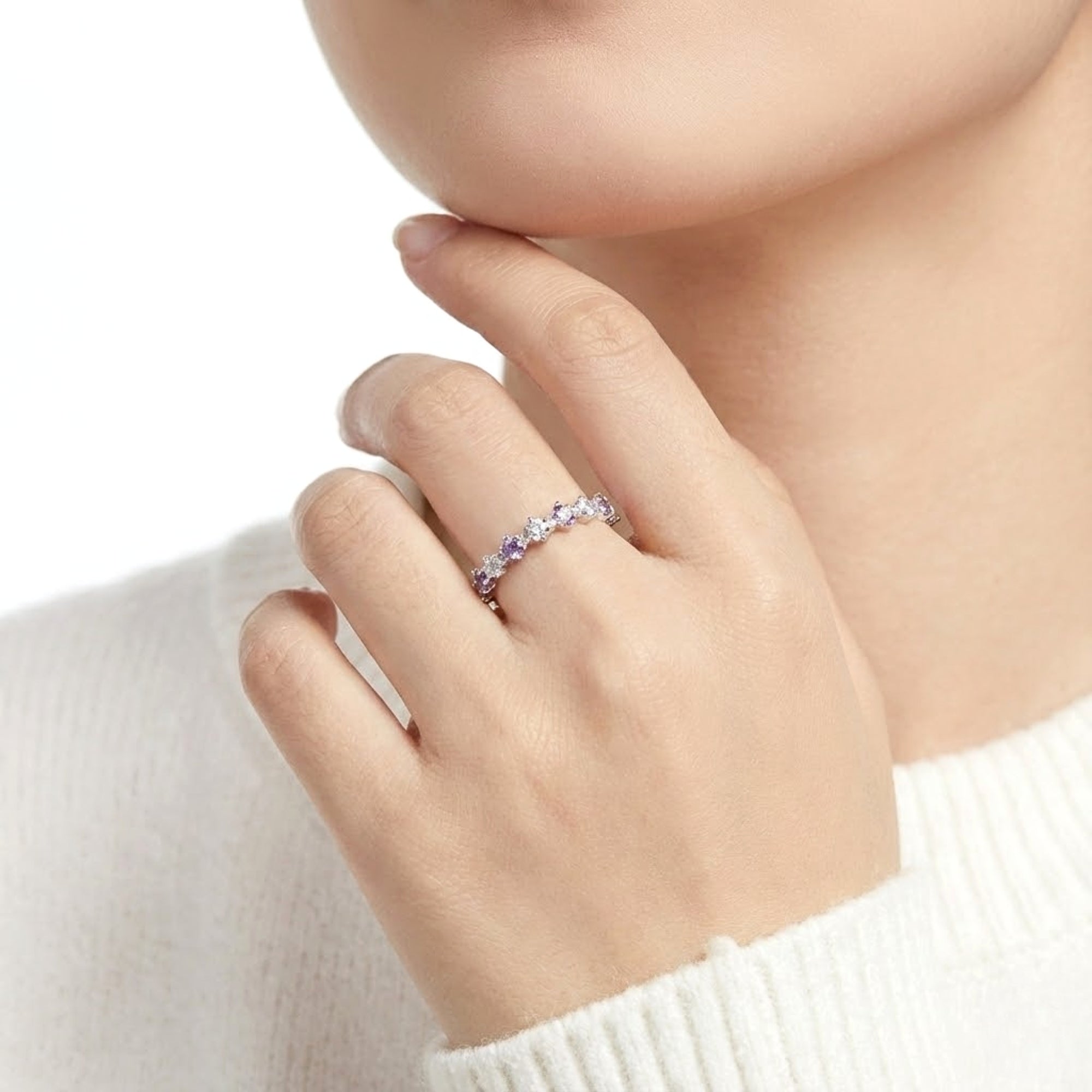 Close-up of a hand wearing the silver amethyst and clear stone eternity ring against a white sweater.