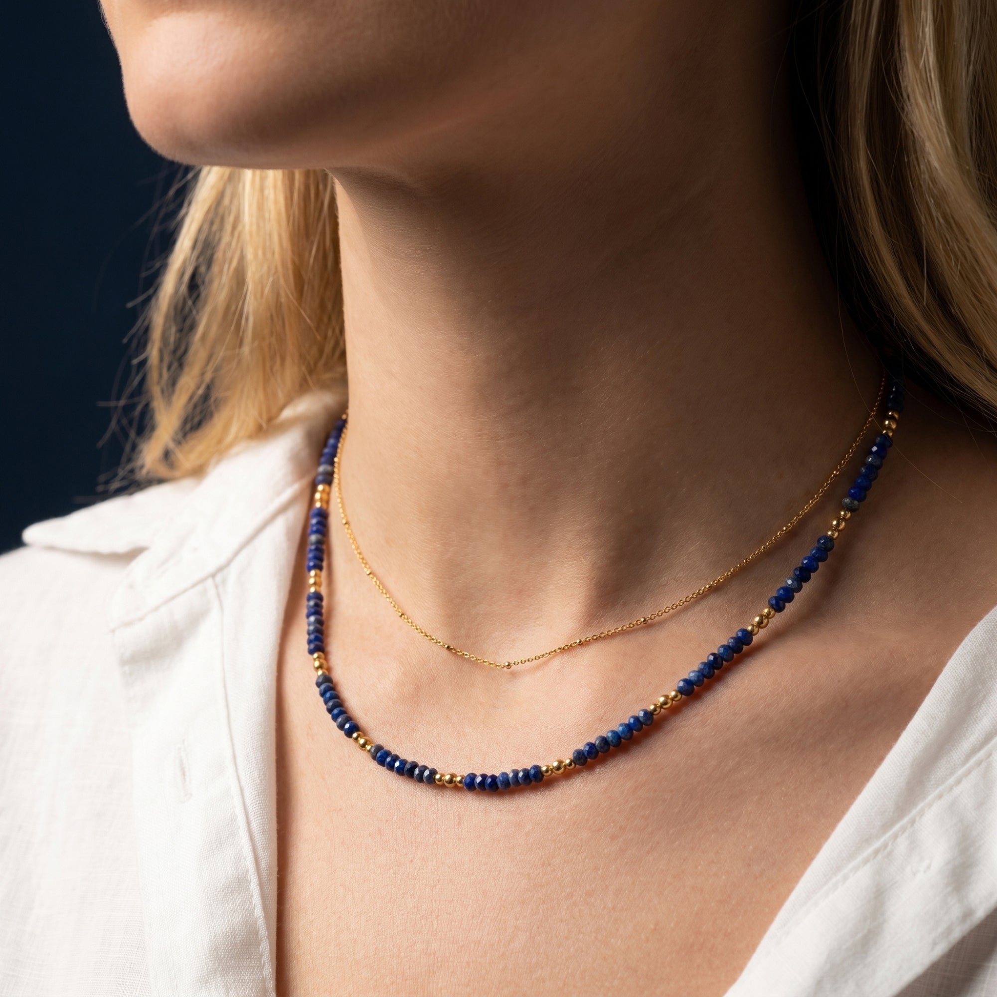 Side view of a model wearing the layered gold and lapis lazuli bead necklace with a white linen shirt.