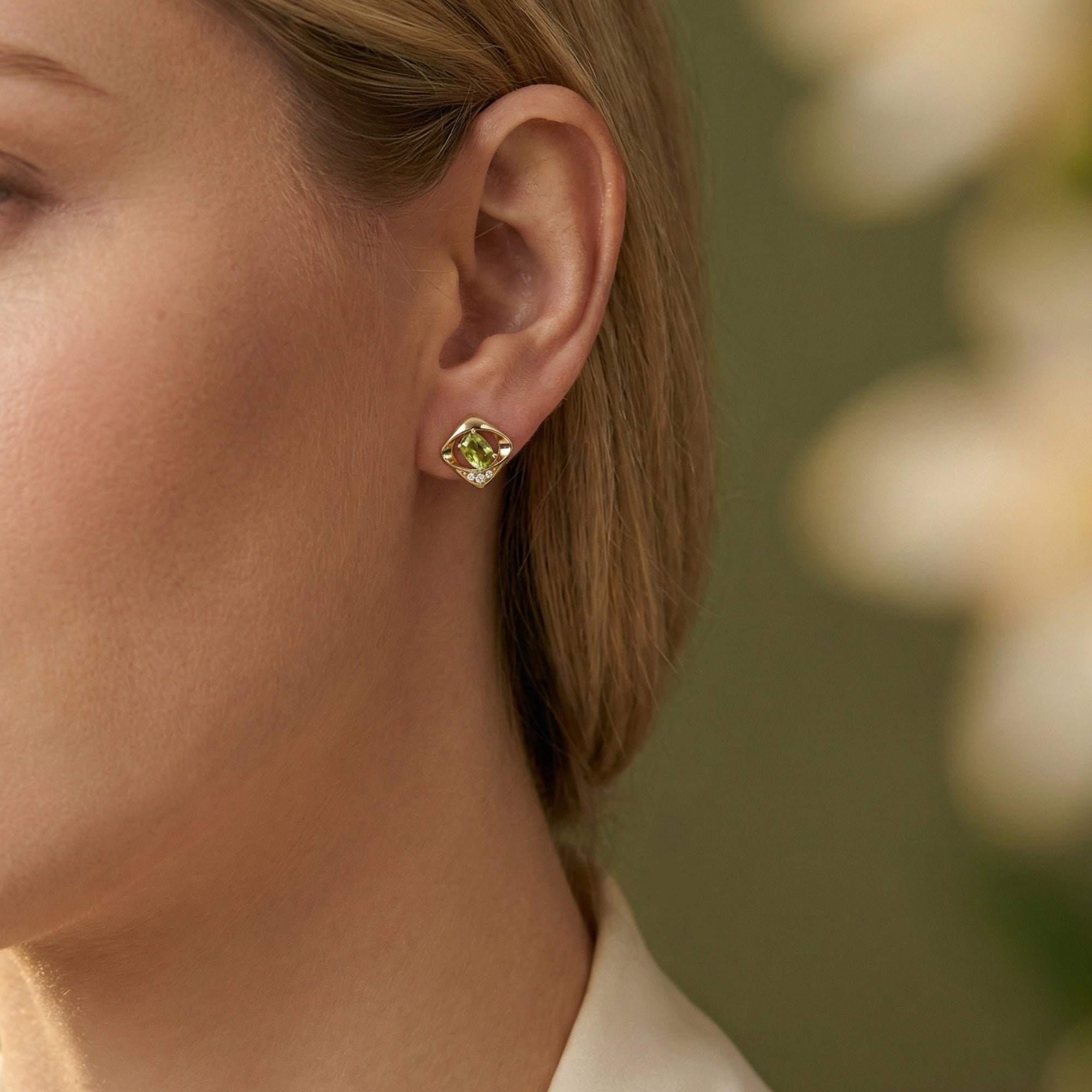 Close-up of a gold vermeil Yvaine stud earring with an oval cut peridot worn on a model's ear.