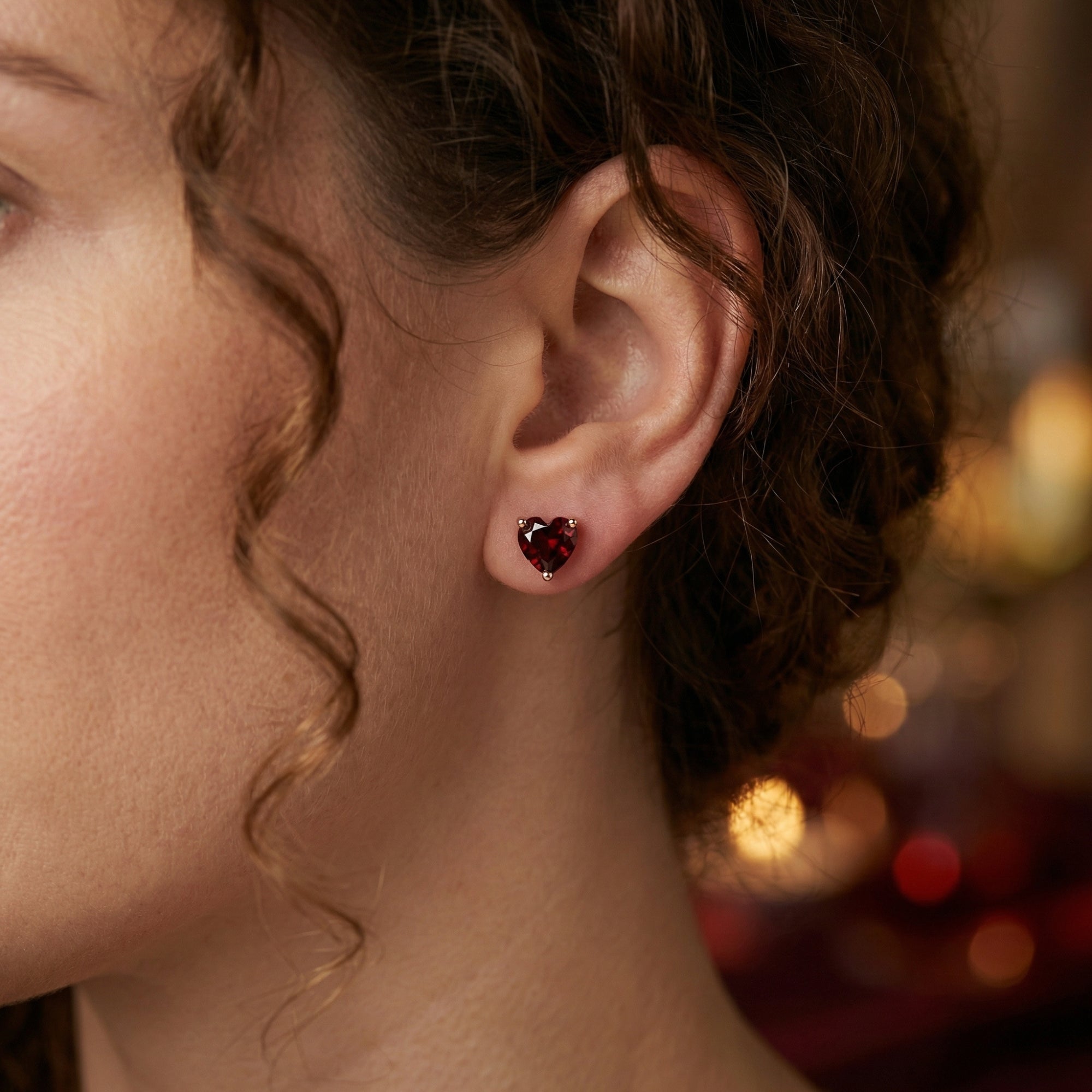 Close-up of a woman wearing the Carissima heart-cut garnet stud earring in 18K rose gold.