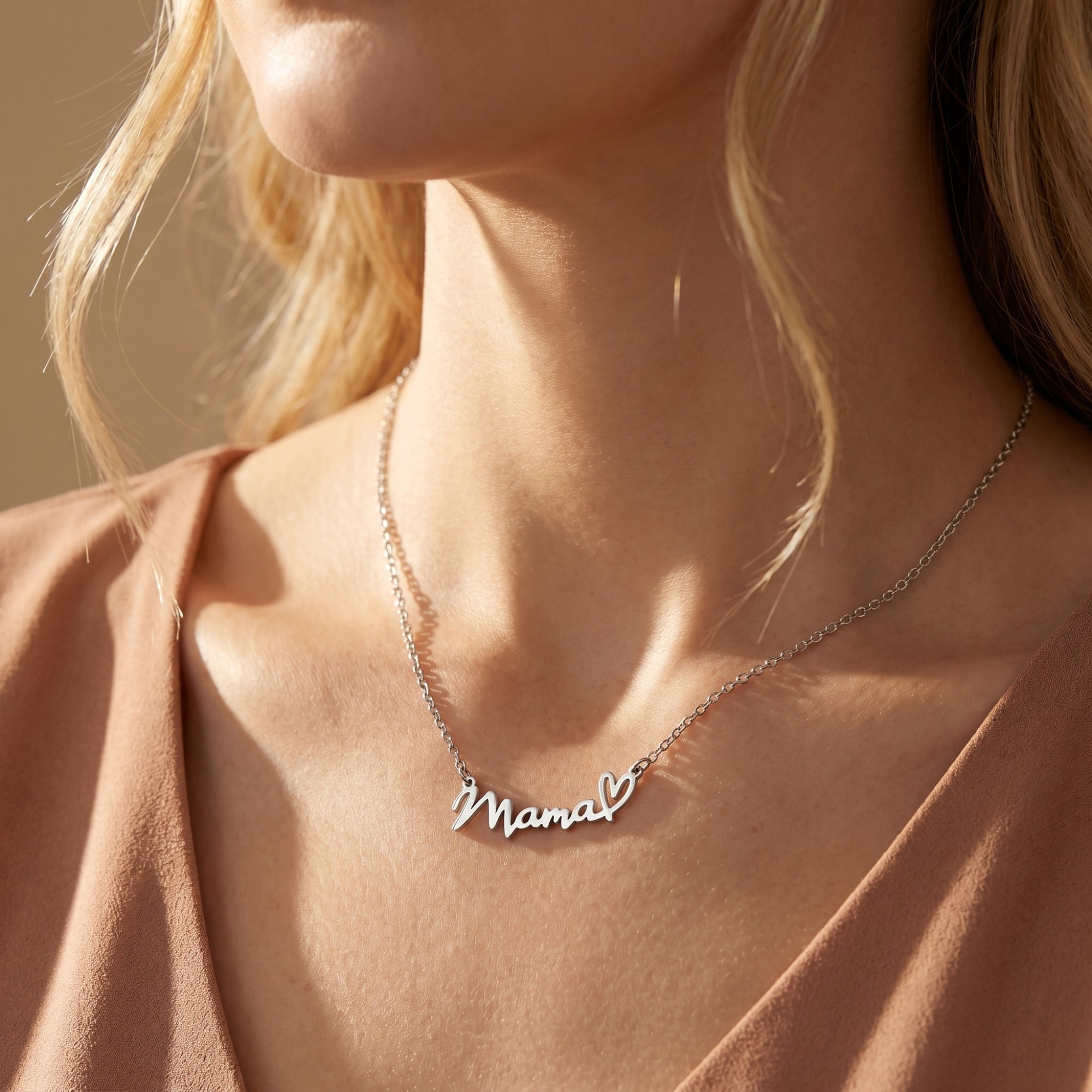 Silver Natalia Mama script necklace with heart motif worn by a model in a mauve top.