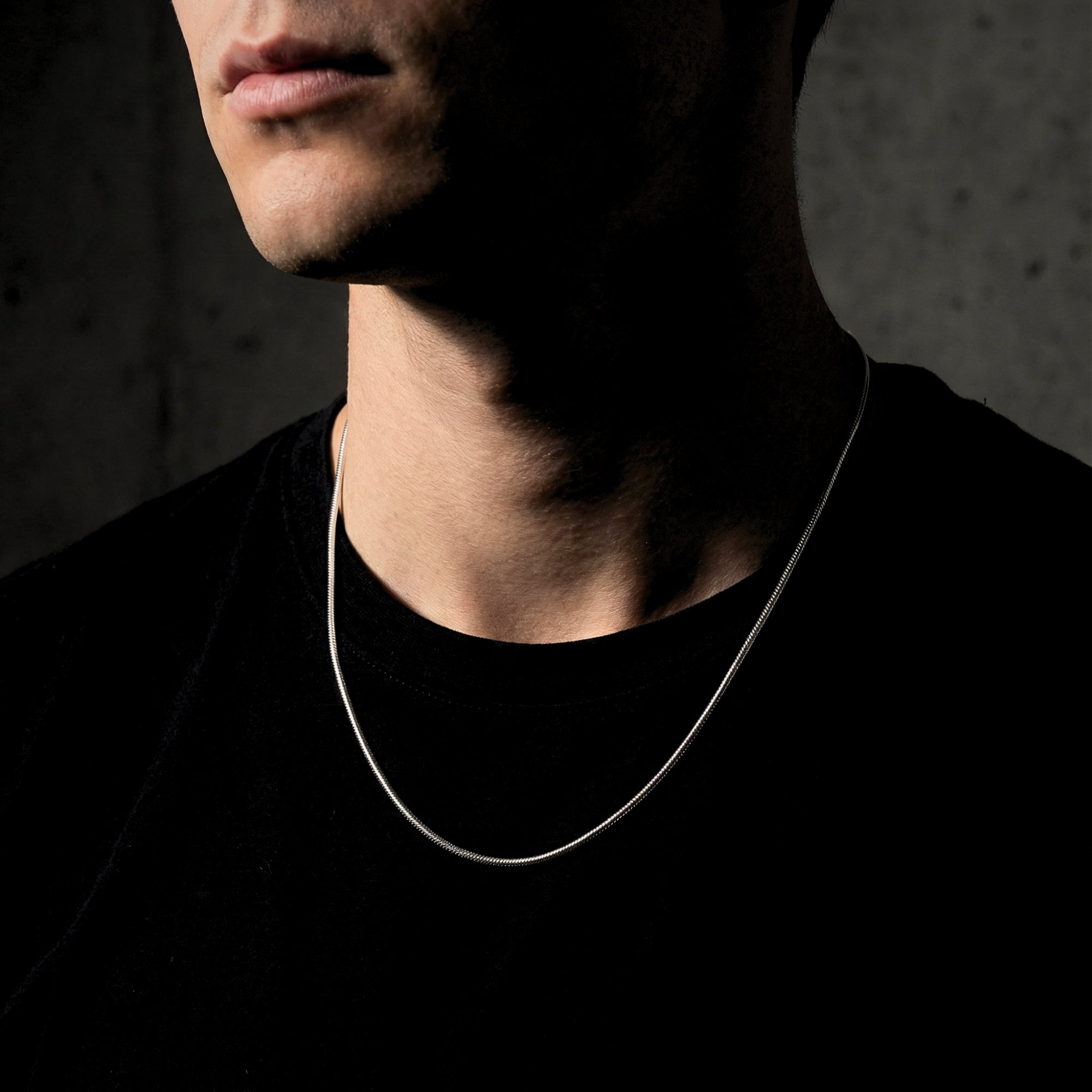 Frontal view of a man wearing a silver stainless steel square link chain necklace against a dark background.