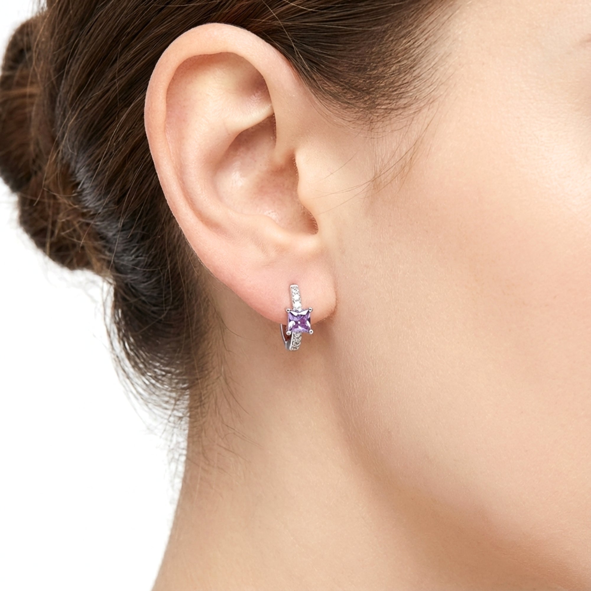 Close-up of a sterling silver huggie earring with a princess-cut purple simulated amethyst on a model's ear.
