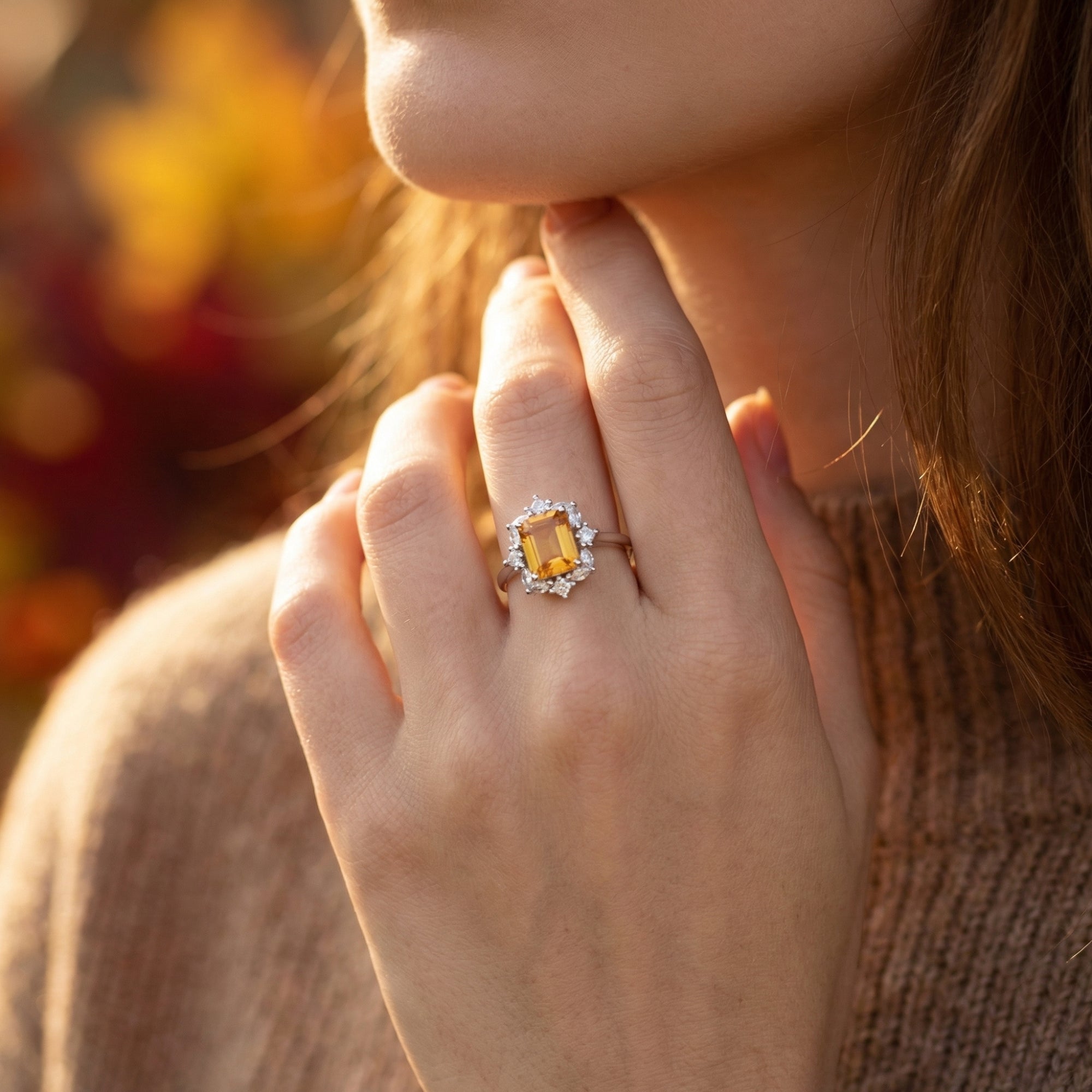 Close-up of a woman's hand wearing a large emerald-cut citrine ring with a silver band and stone halo.