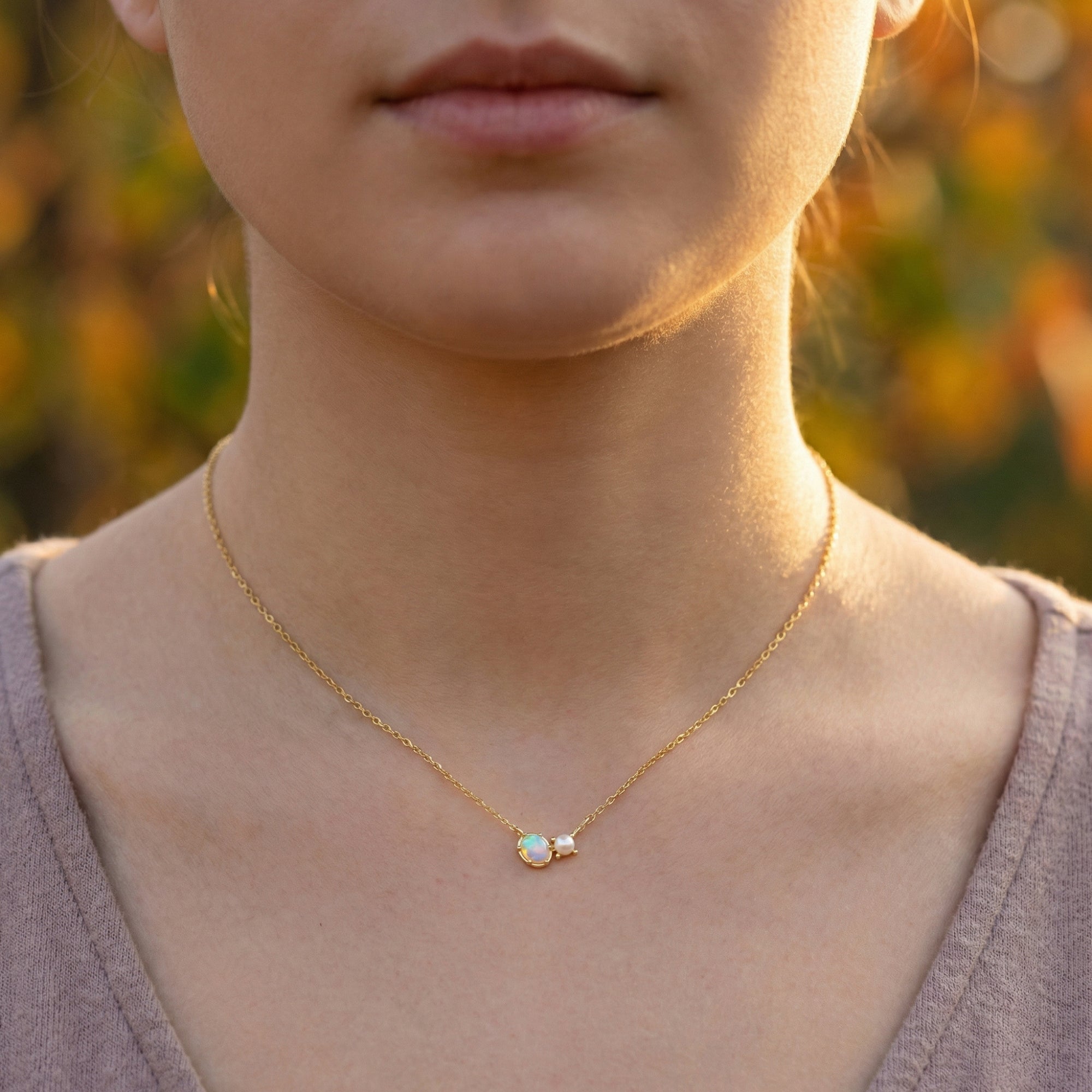 Front view of a woman wearing the gold Lumira oval white opal and pearl pendant necklace.