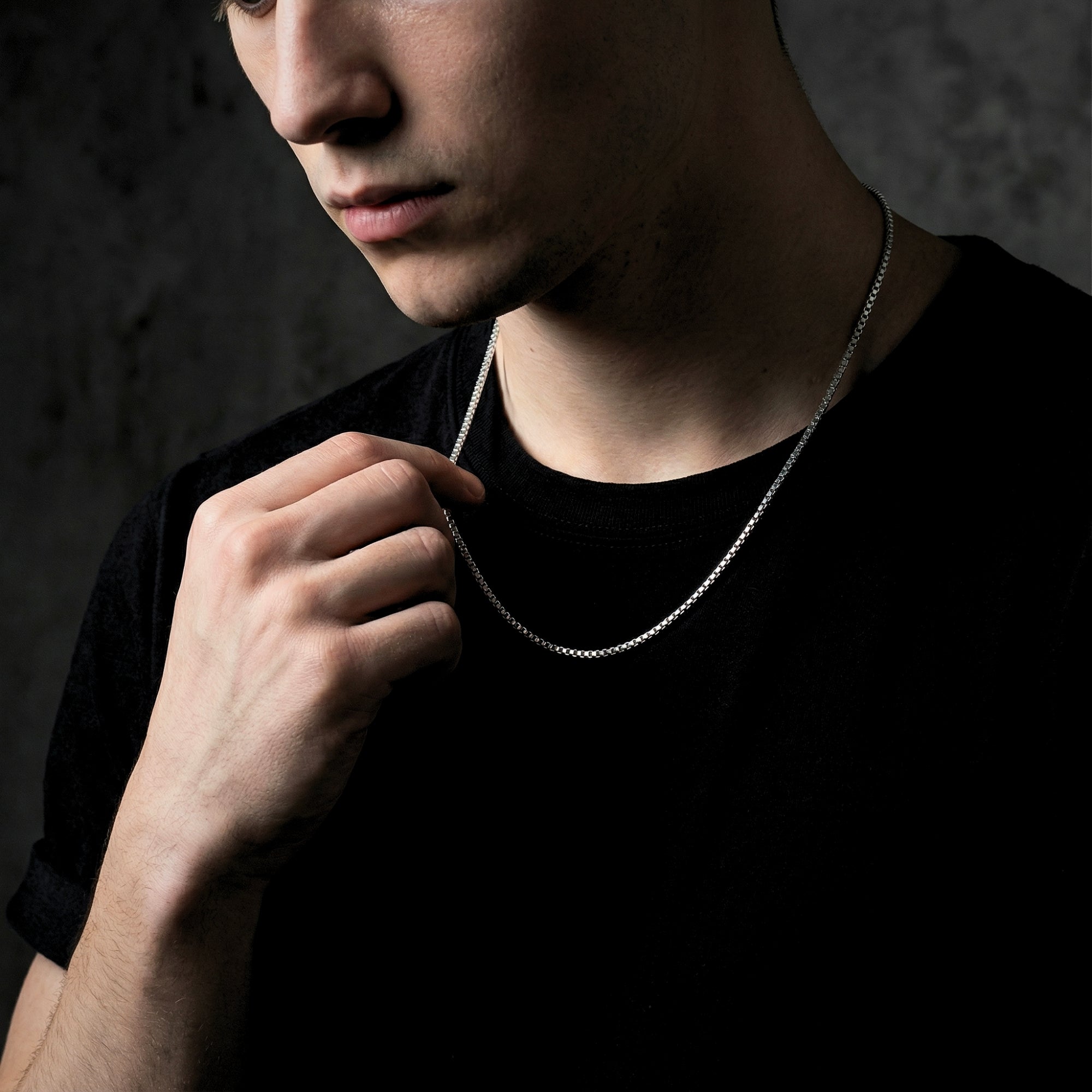 Male model adjusting a silver stainless steel boxer chain necklace while wearing a black t-shirt.