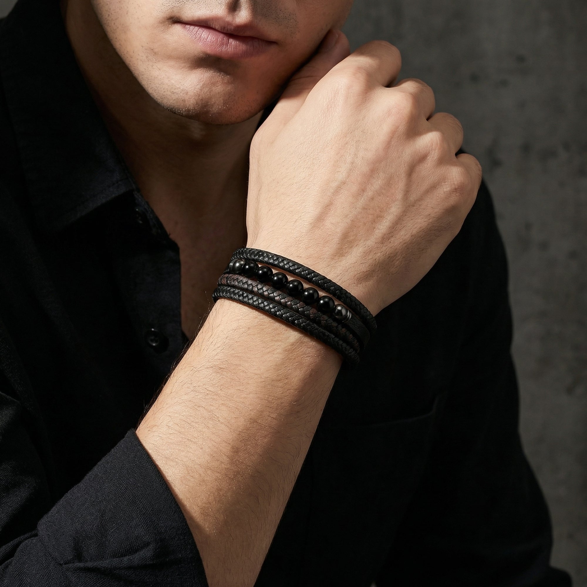Men's multi-strand braided leather bracelet with black beads and black finish clasp worn on a man's wrist.