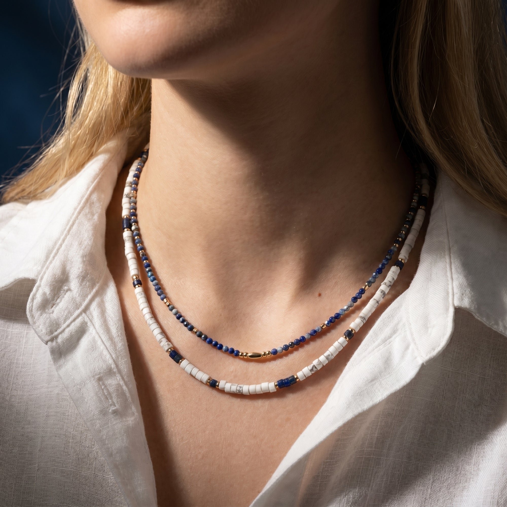 Layered natural lapis lazuli and white bead necklace set with gold-plated accents worn by a model.