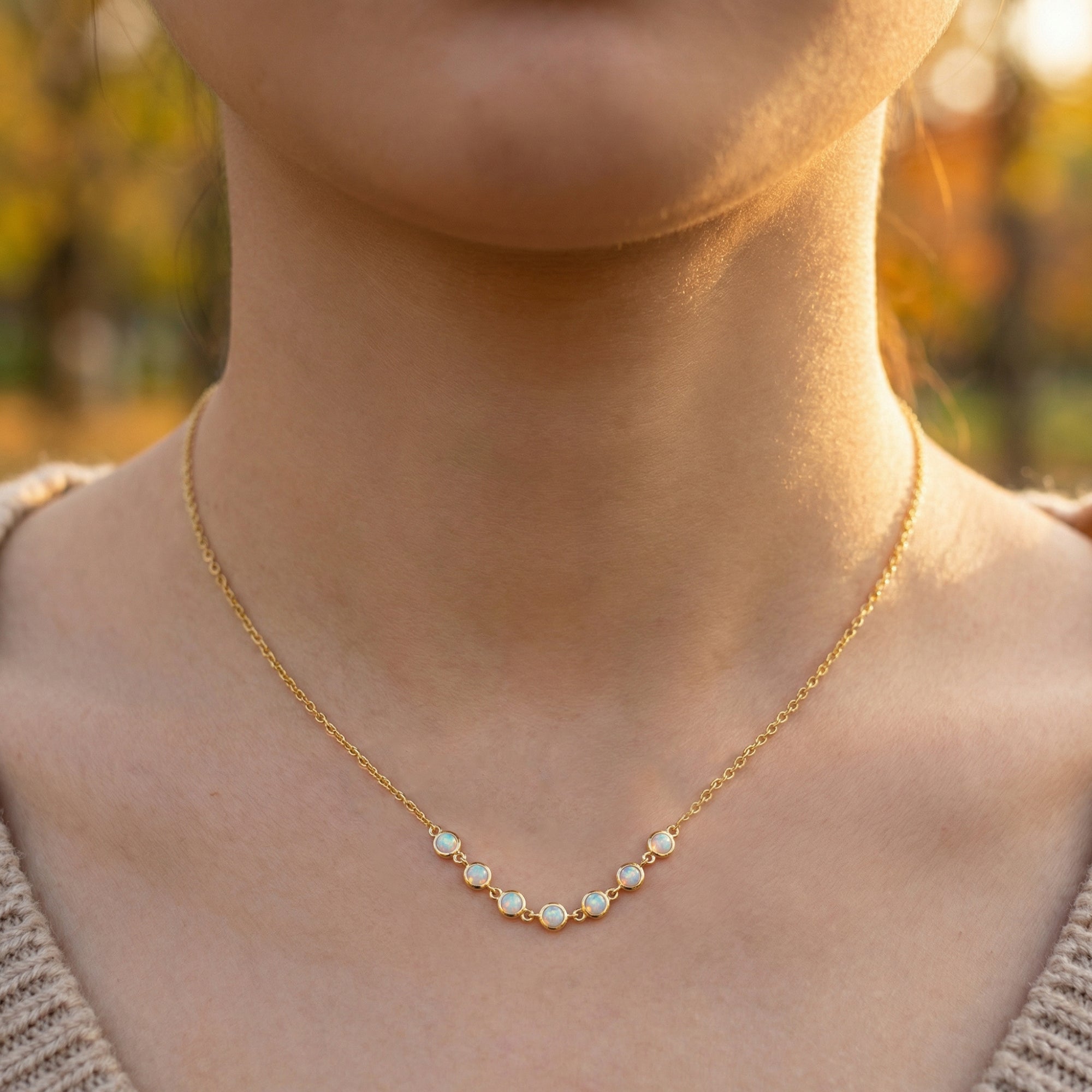 Front view of the gold-tone Lumina necklace with seven natural white opals worn on a woman's neckline.
