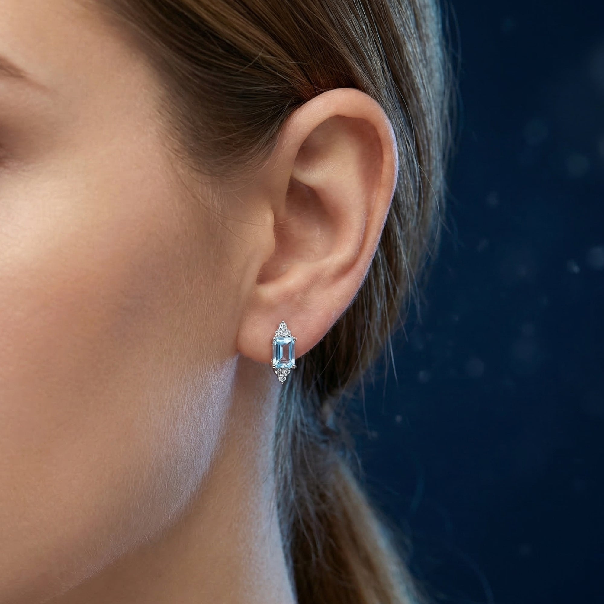 Profile view of a model wearing a sterling silver earring with a faceted emerald cut natural topaz.