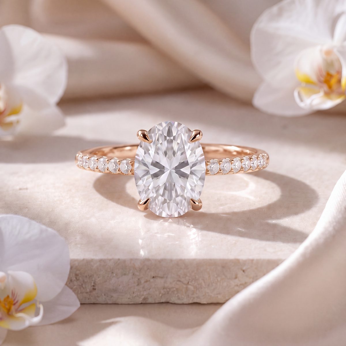 Rose gold oval-cut moissanite engagement ring with a pavé band displayed on a pedestal.