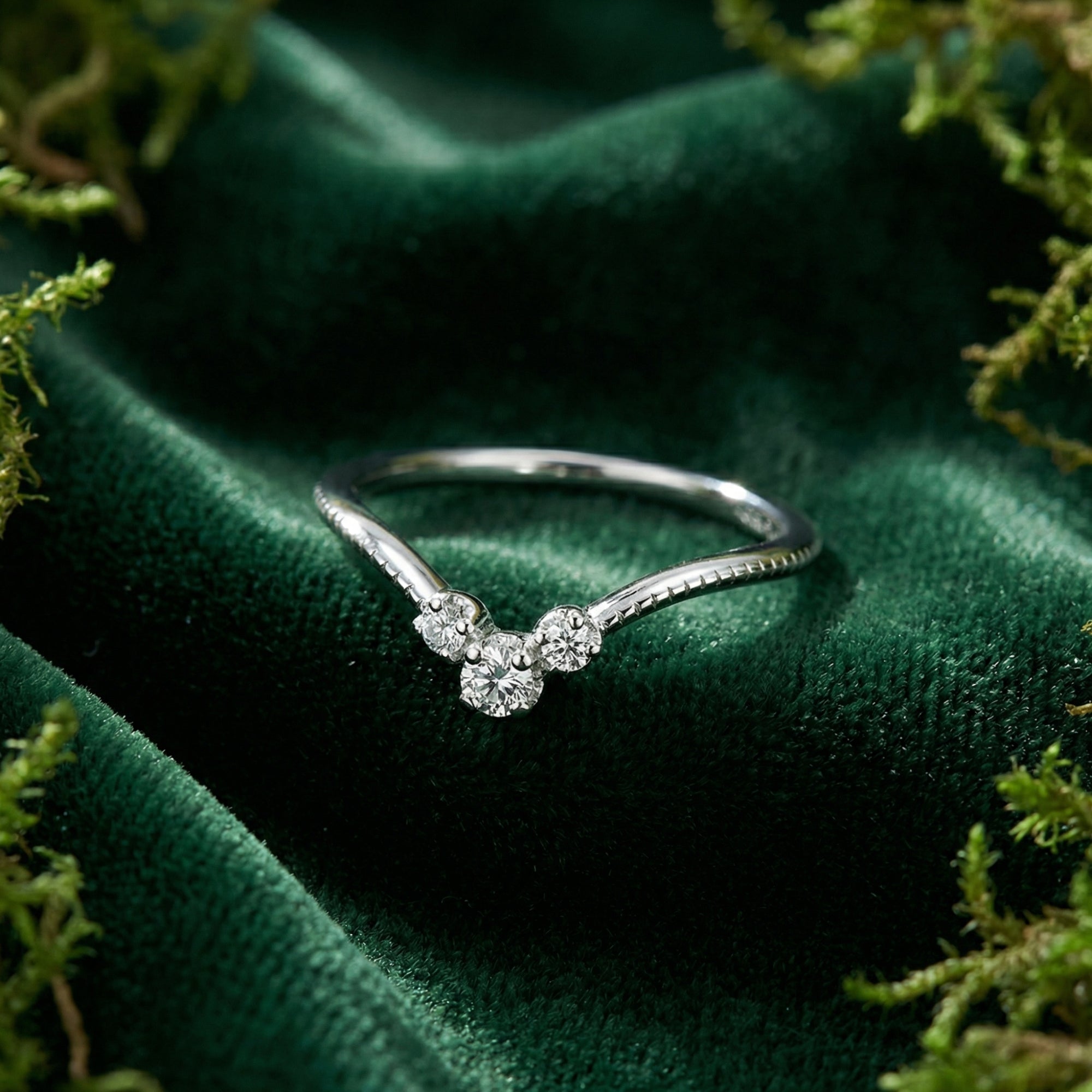 Sterling silver curved wedding band with diamond accents on a green velvet background with moss.