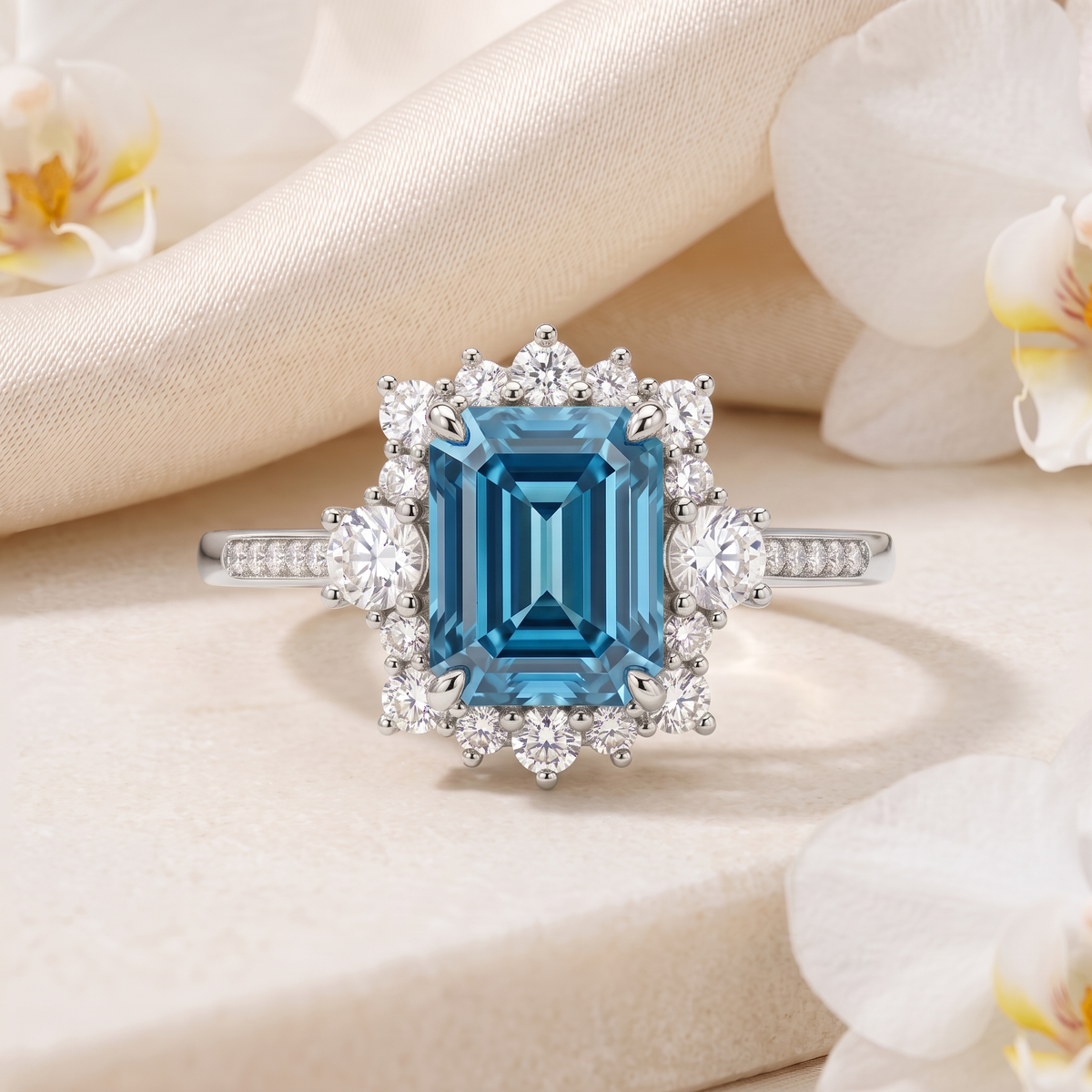 White gold emerald-cut blue moissanite halo ring resting on a neutral stone pedestal.