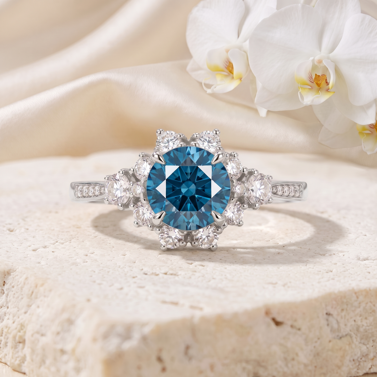 White gold halo engagement ring featuring a round blue moissanite center stone and diamond cluster setting.