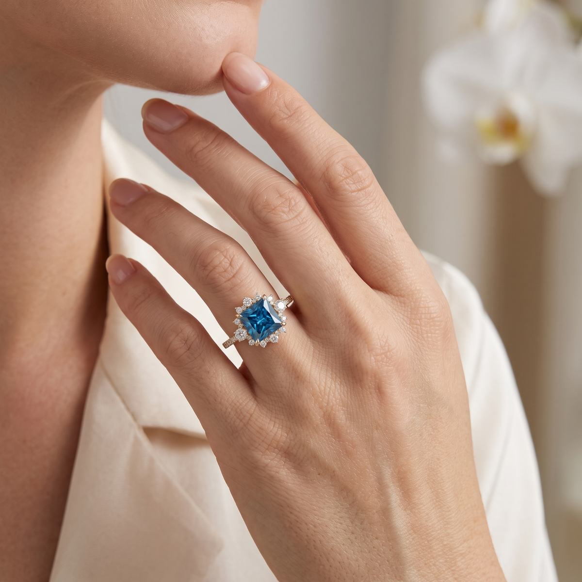 Close-up of a hand wearing the princess-cut blue moissanite halo engagement ring in rose gold.
