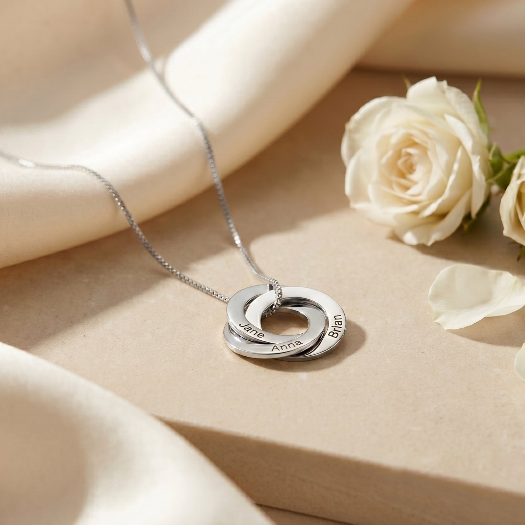 Silver Camilla necklace with three interlocked engraved rings on stone with white roses.