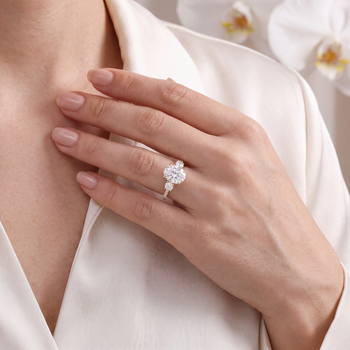 Yellow gold three-stone oval moissanite ring styled on a woman's hand.