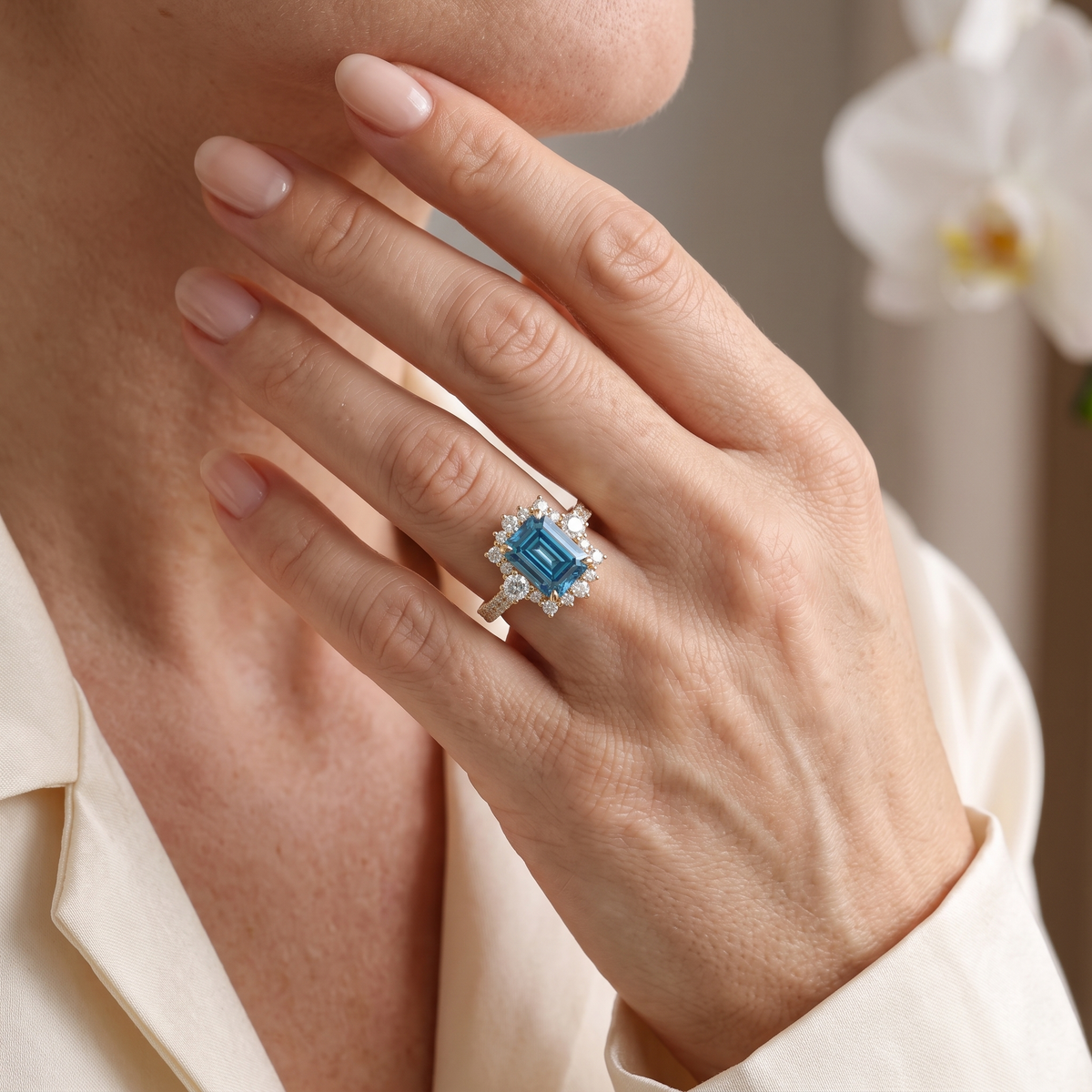 Close-up of a woman wearing an emerald-cut blue moissanite halo ring in rose gold.