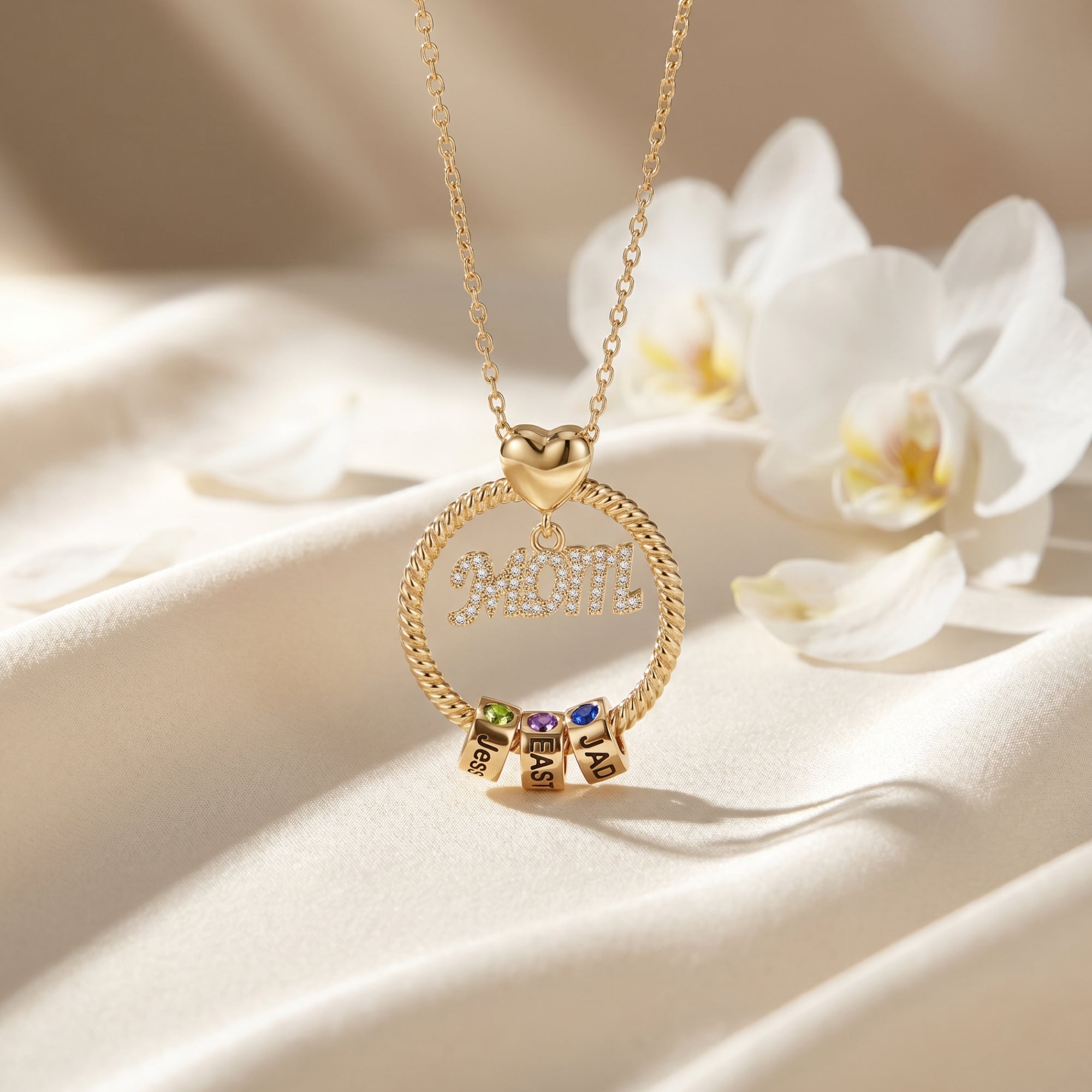 Close-up of a gold Kalisene necklace showing the twisted-circle MOM pendant and engraved name rollers.