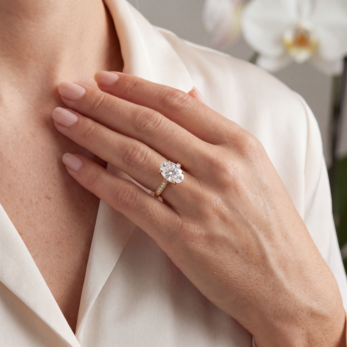 A woman wearing a yellow gold oval moissanite engagement ring resting her hand near her collarbone.
