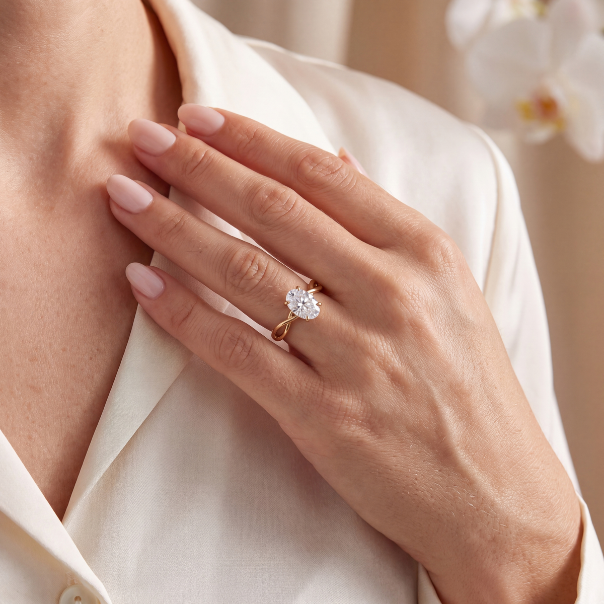 Lifestyle portrait of a woman wearing a yellow gold oval moissanite ring with her hand resting on her chest.