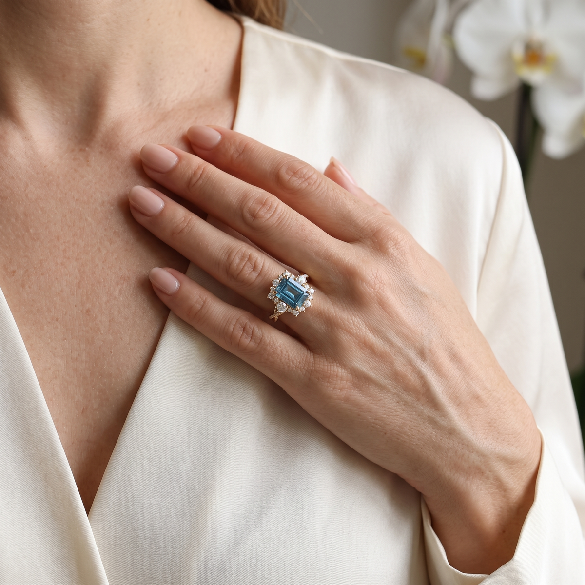 Close-up view of model wearing an emerald cut blue moissanite halo engagement ring in rose gold