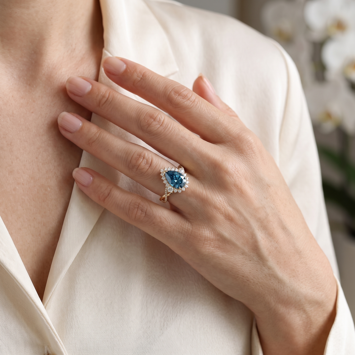 Close-up of a model wearing a pear cut blue moissanite halo engagement ring in rose gold.