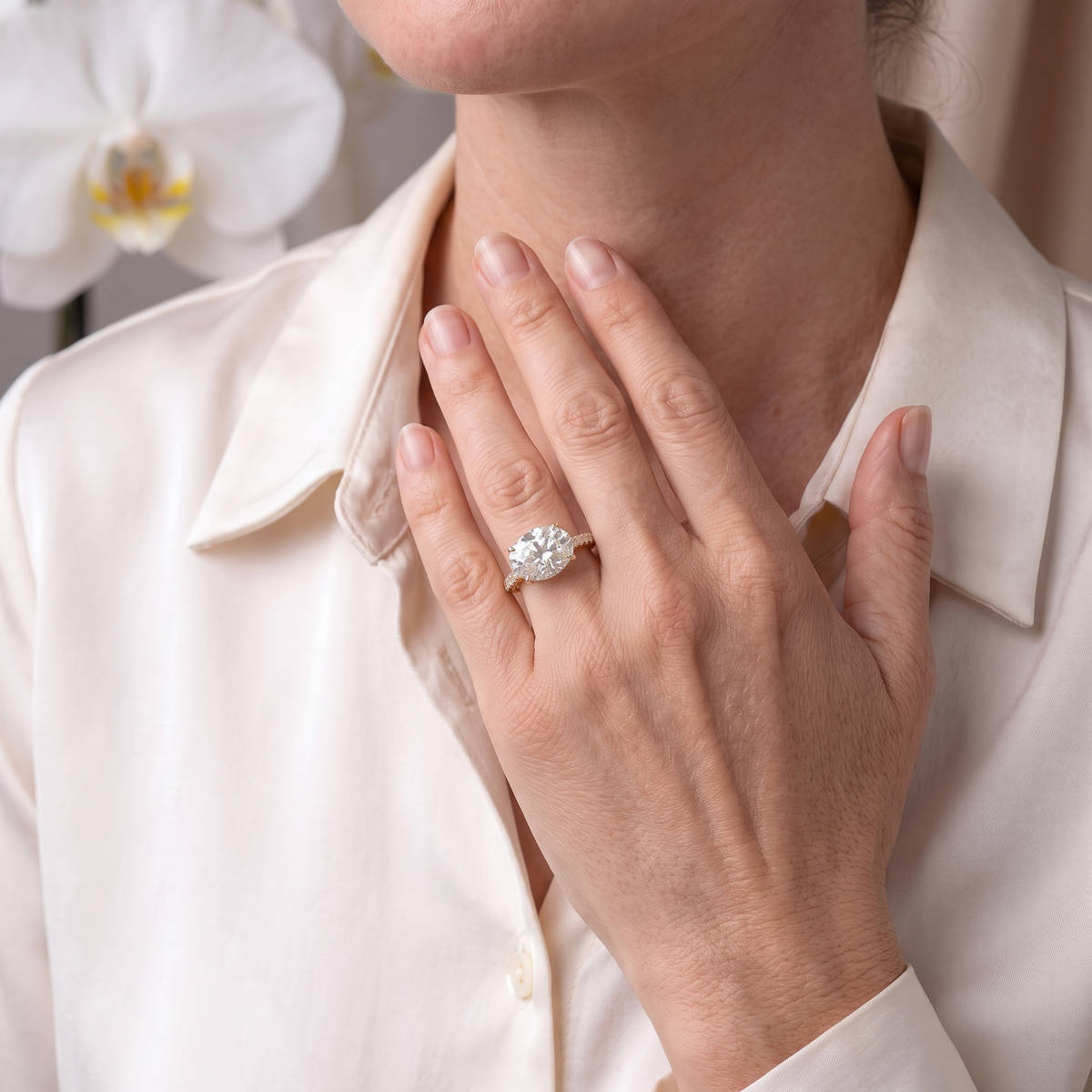 A close-up lifestyle view of an East-West oval cut moissanite engagement ring in yellow gold worn on a hand.